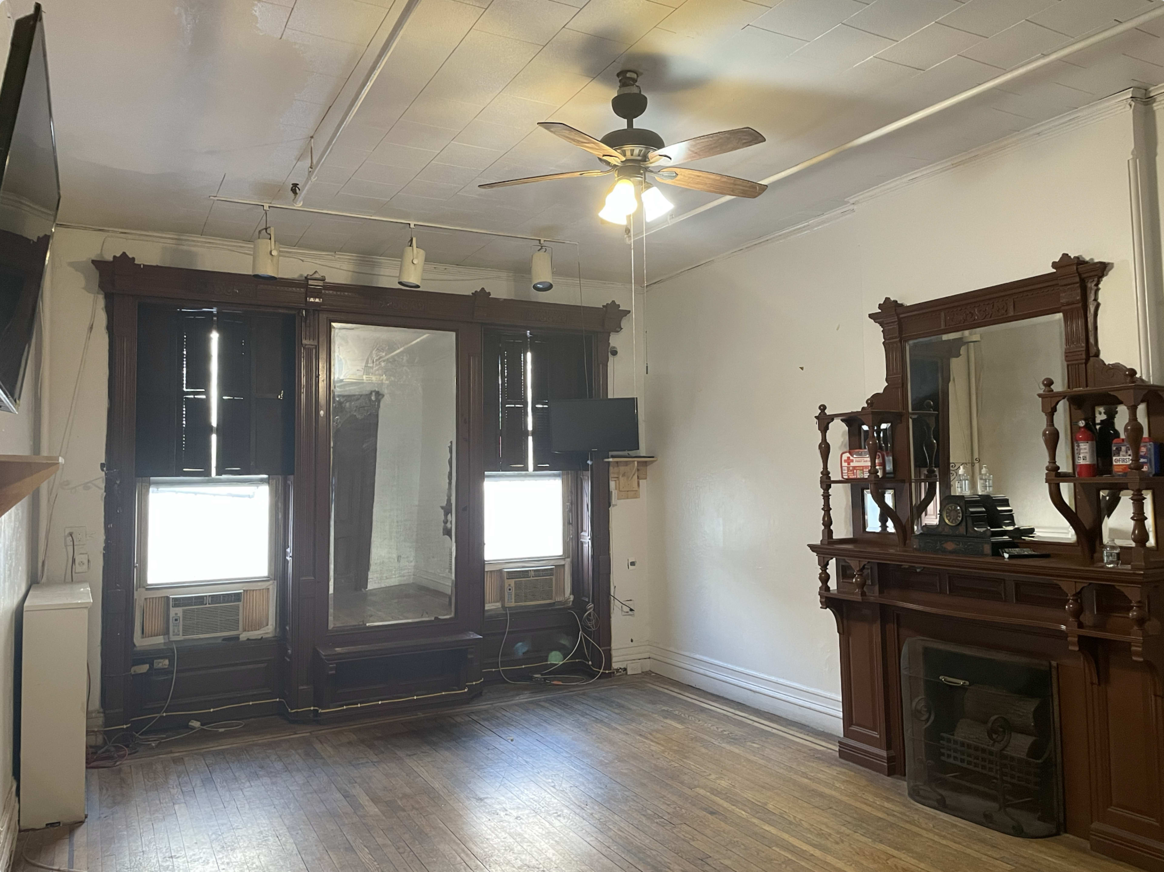 The room features wooden accents, two air conditioning units under windows, a ceiling fan, and a decorative fireplace.