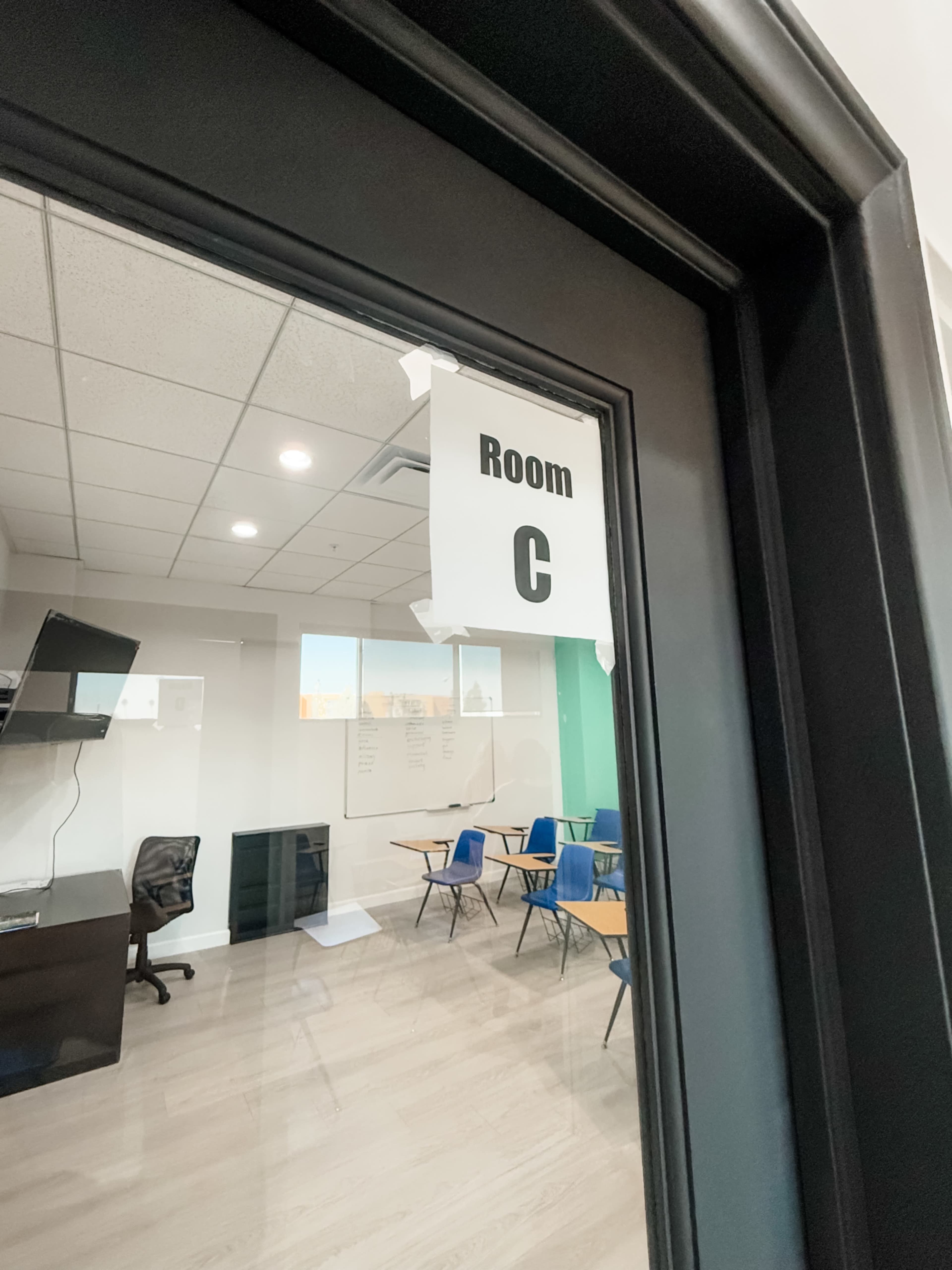 A sign on a glass door indicates that the room is labeled "Room C," with empty desks and chairs visible inside.