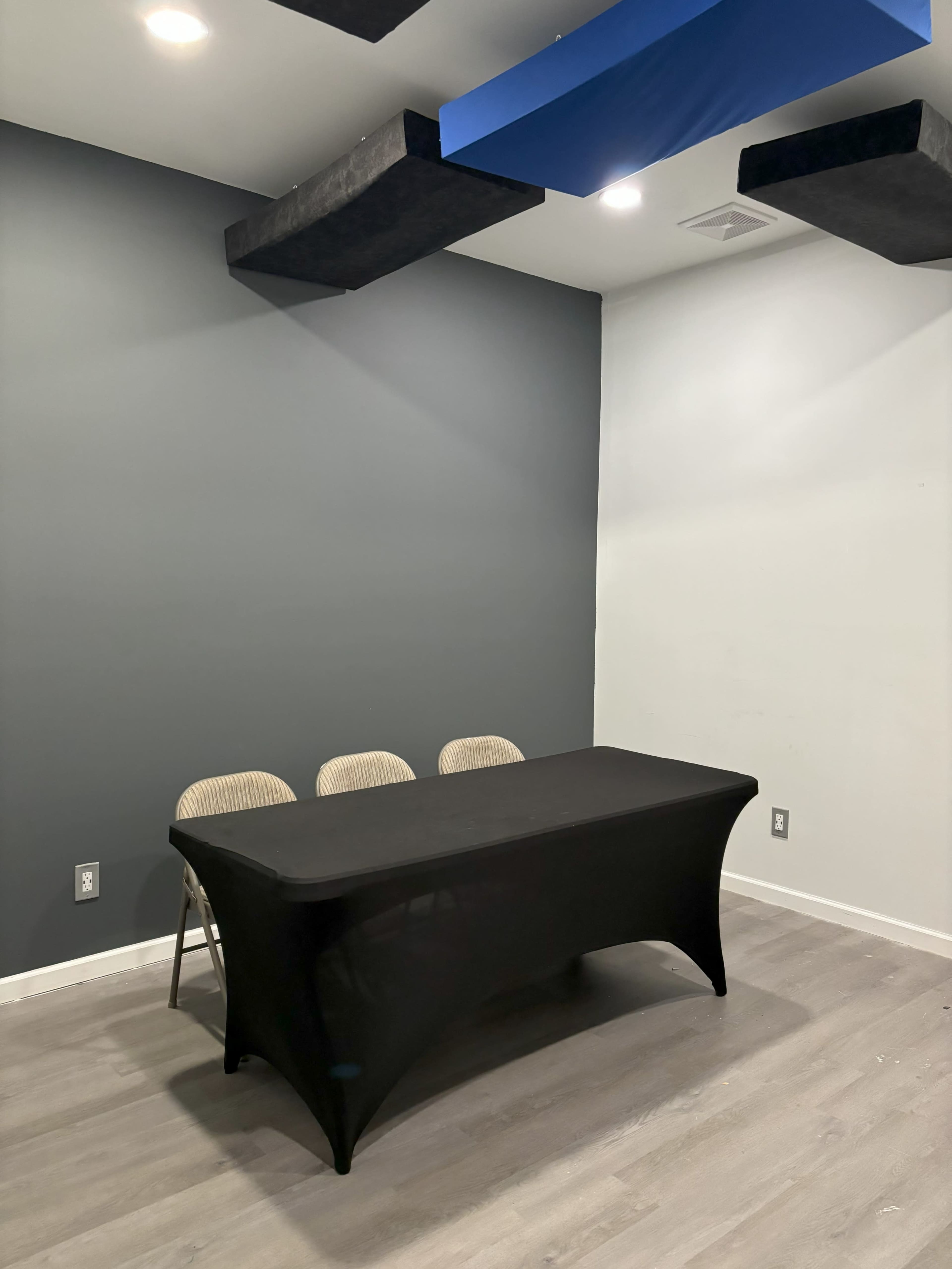 The image shows a small room with a black table and three chairs against a wall painted in two shades of gray.