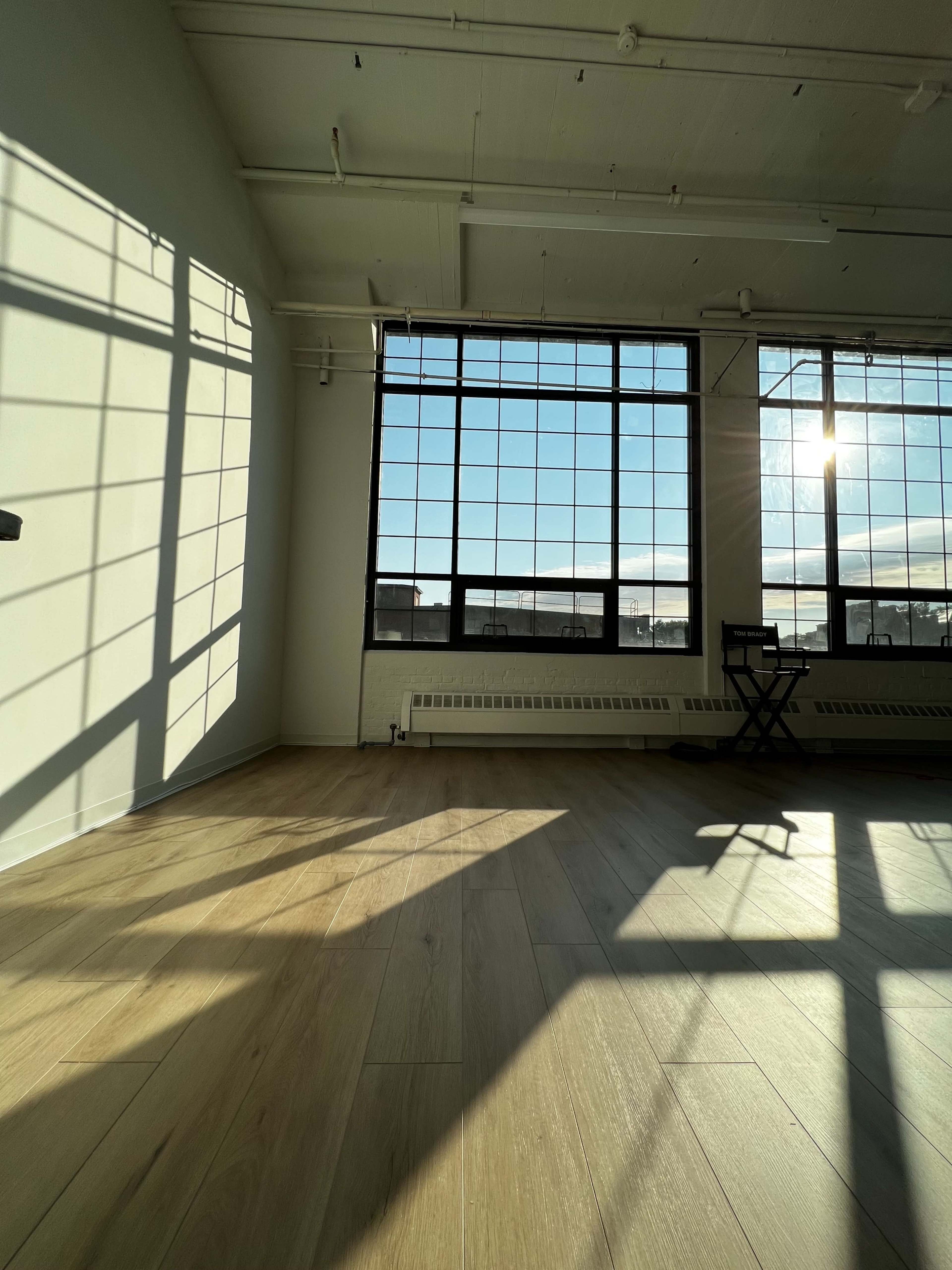 A spacious room with large windows casting shadows on the wooden floor.