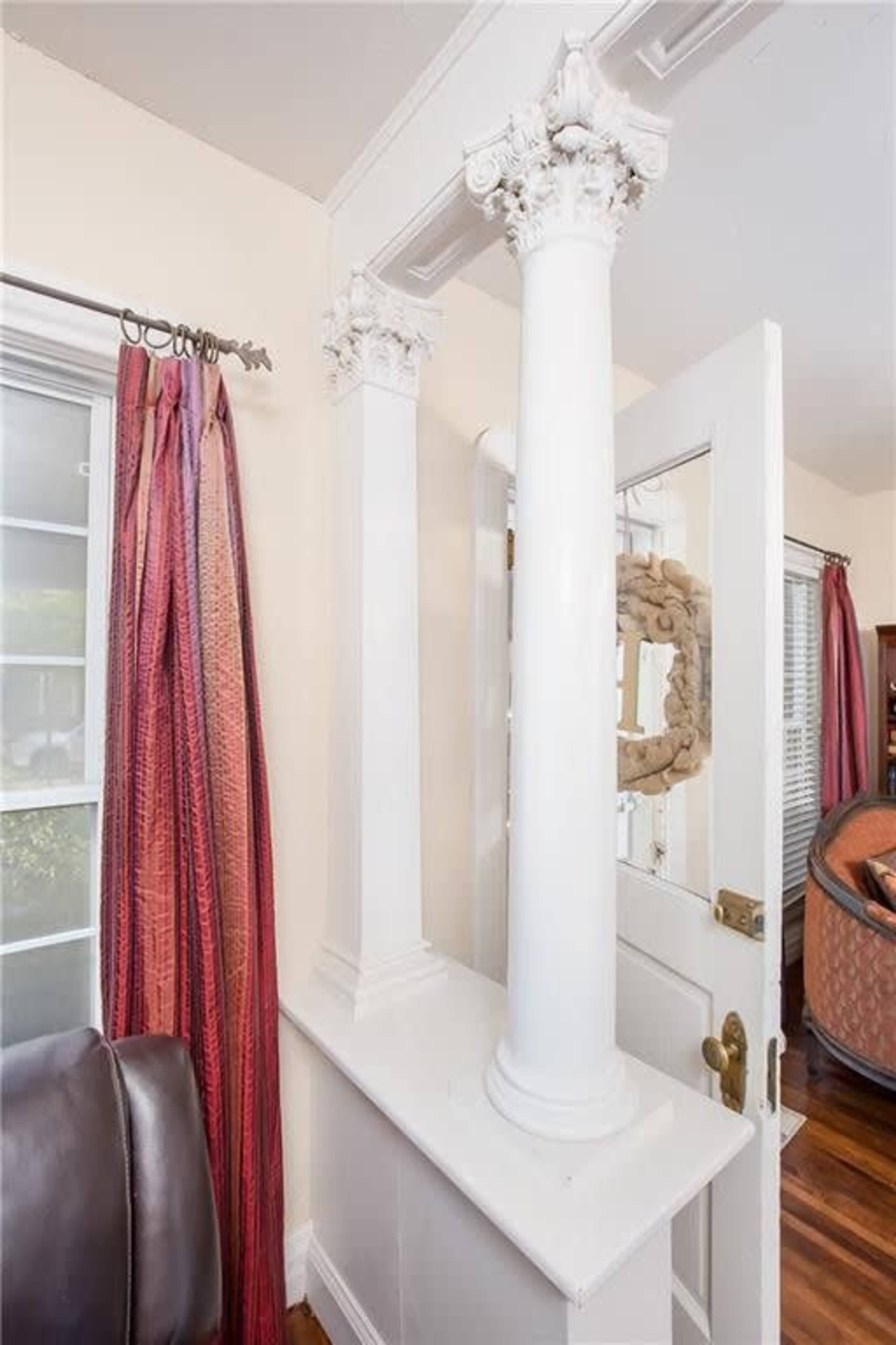 The image shows a corner of an interior space featuring two white columns, a doorway, and red curtains on a window.