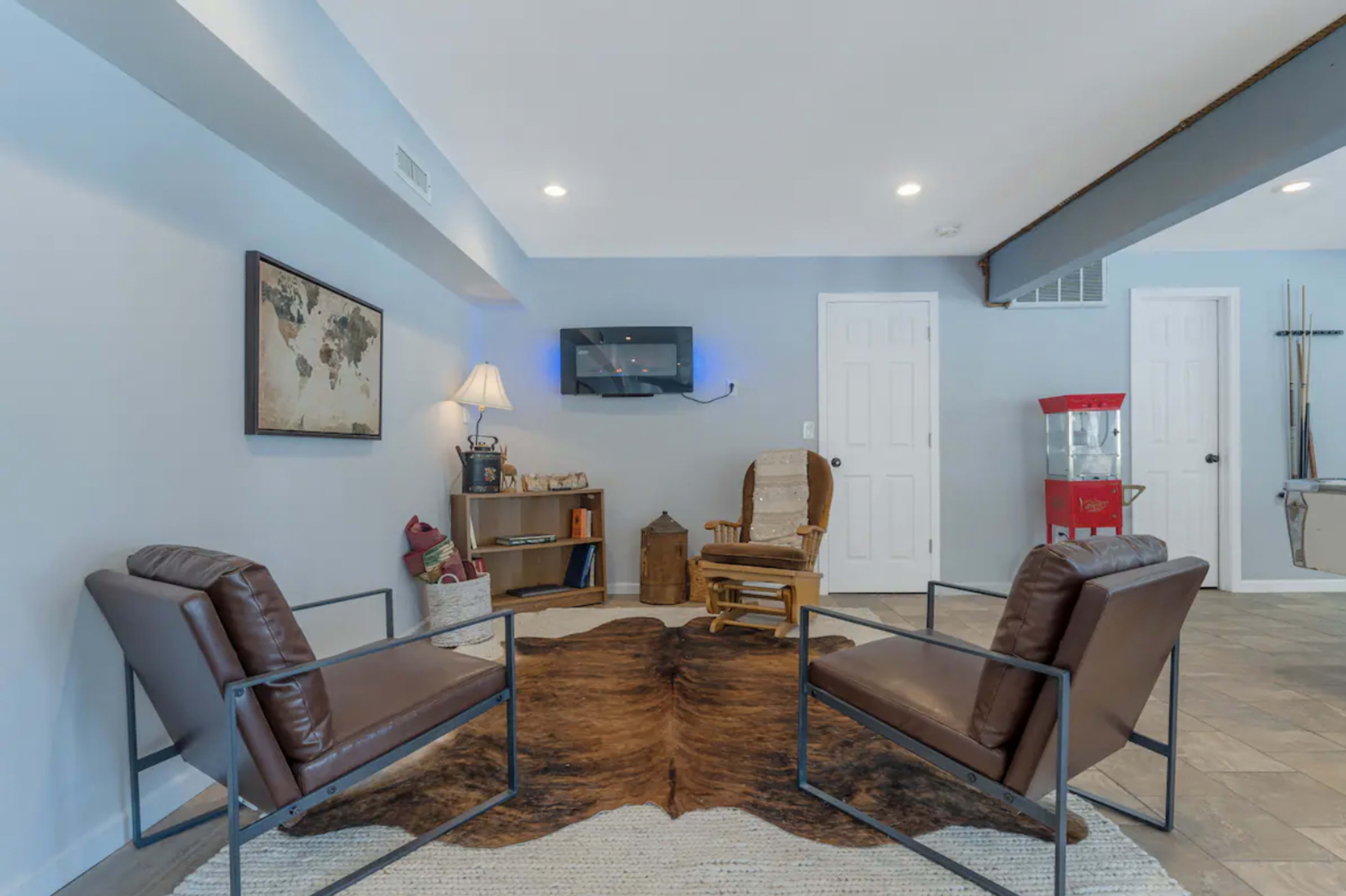 A cozy seating area features two leather chairs, a wooden rocking chair, a small bookshelf, and a vintage popcorn machine against a light blue wall.