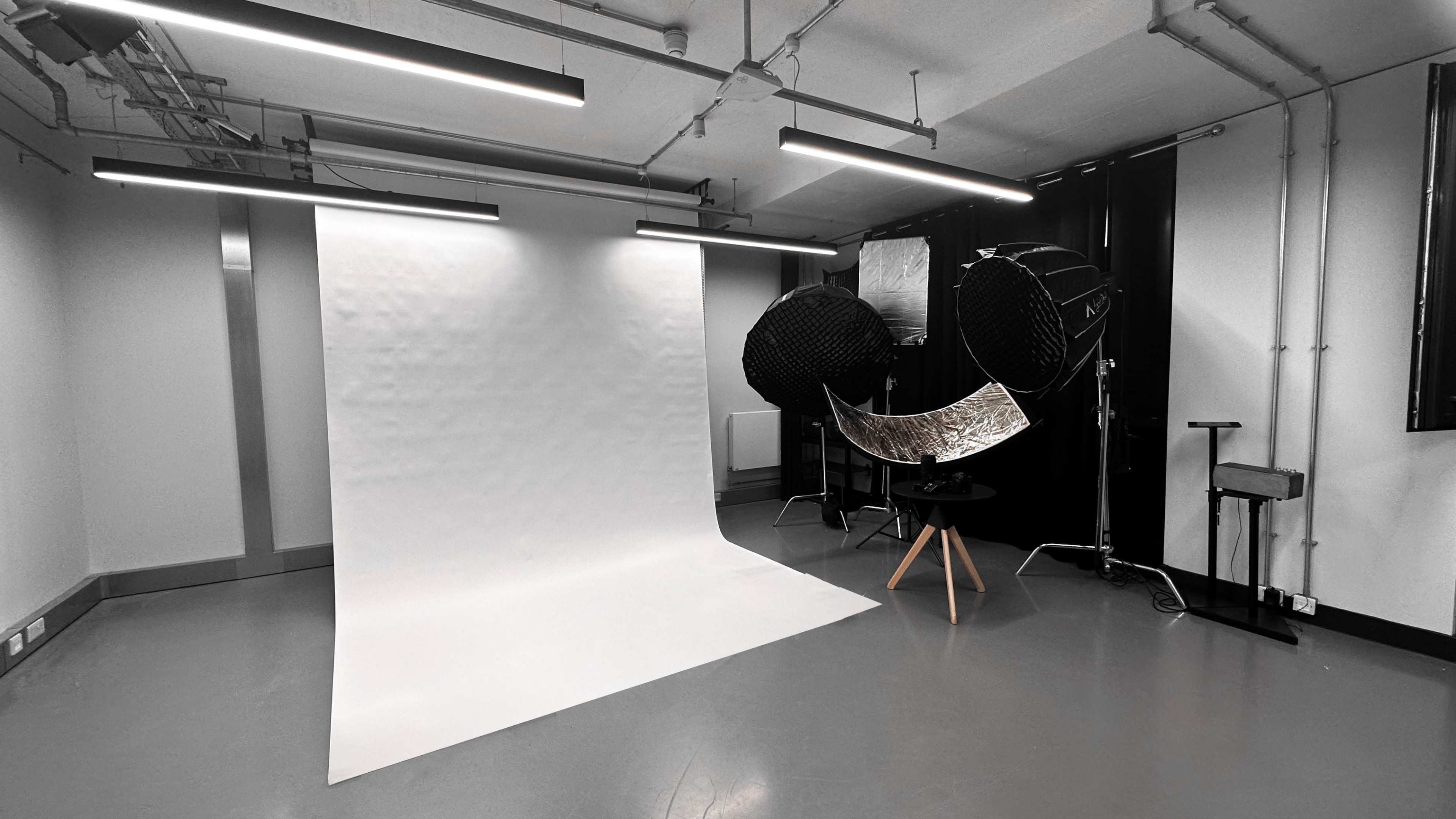 A photography studio with a white backdrop, large softbox lights, and a round reflector on a tripod.