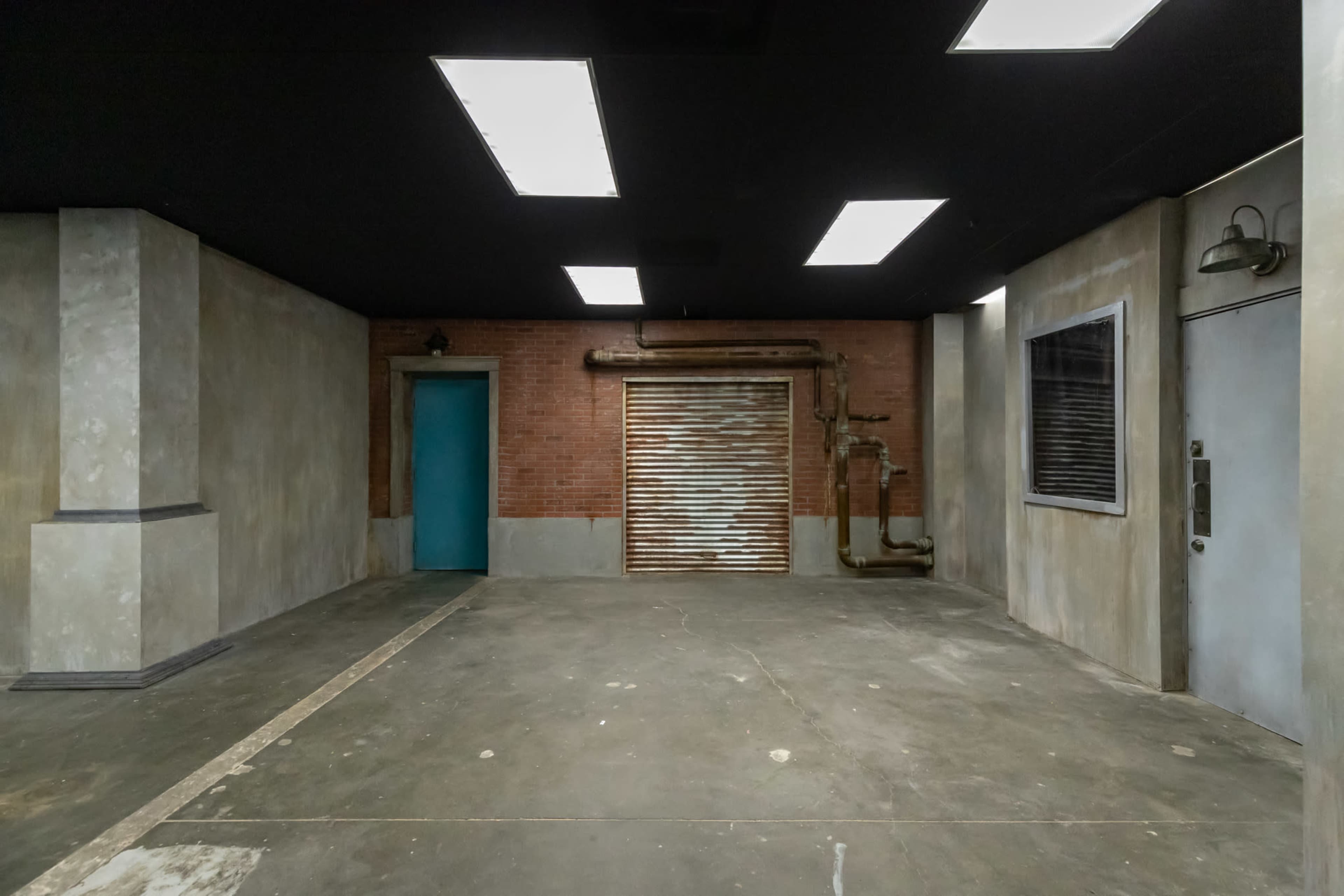 The image shows an industrial-style room with exposed brick walls, a shuttered door, and a blue door on the left.