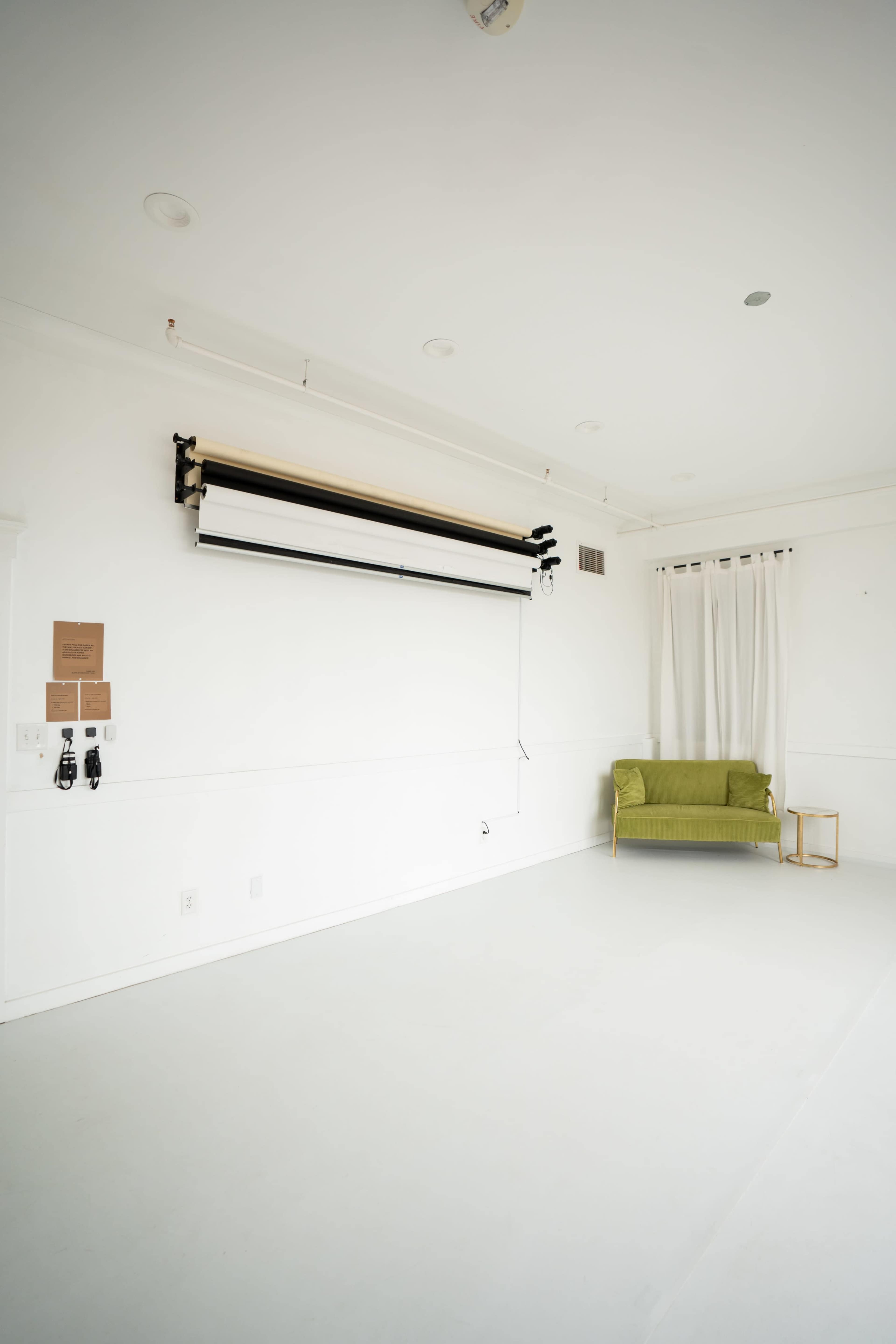 The image shows a minimalistic, bright studio space with a green couch, a rolling backdrop, and a curtain against a white wall.
