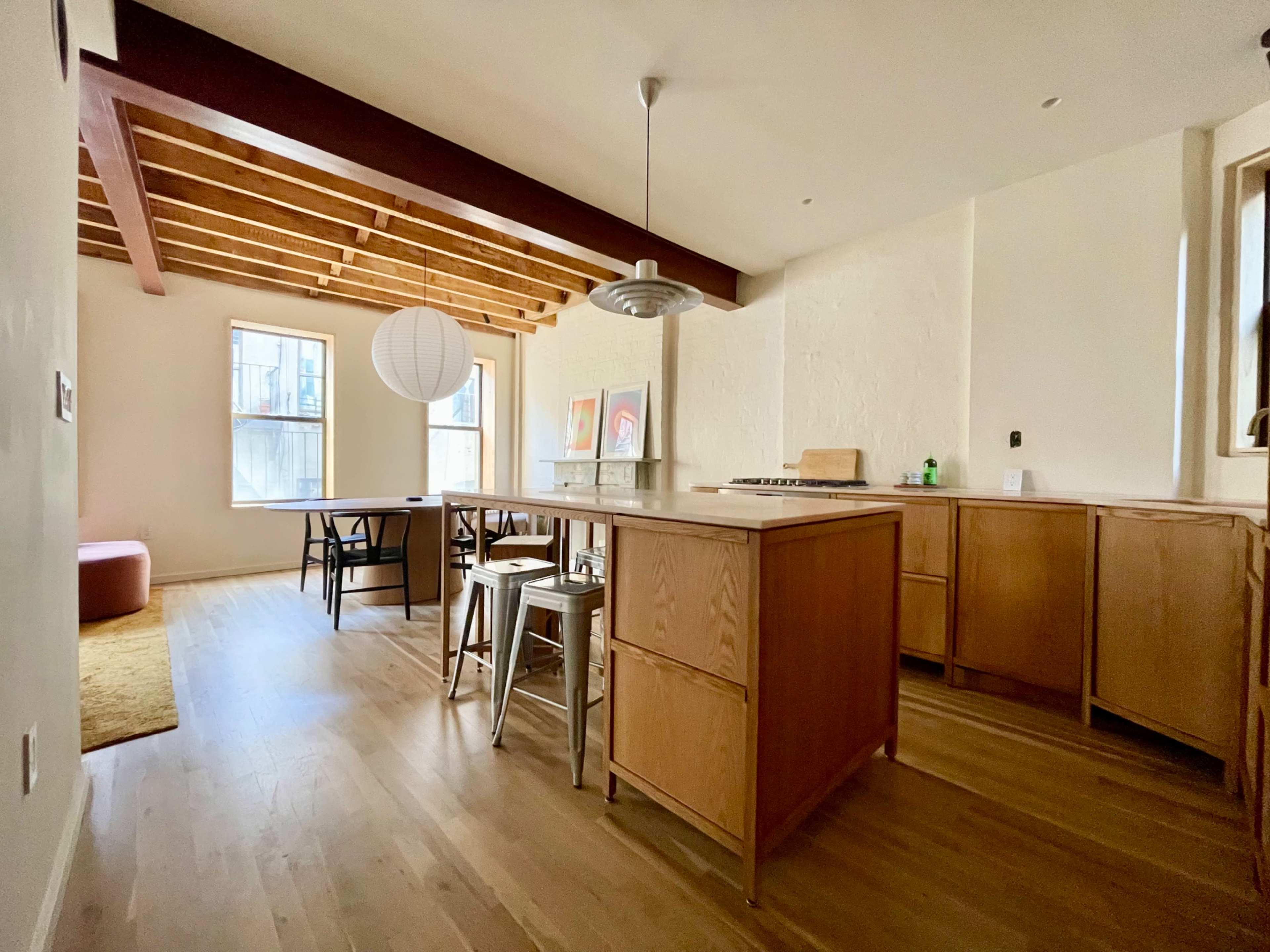 The image shows a modern kitchen and dining area with wooden beams, a central island, and a dining table surrounded by chairs.