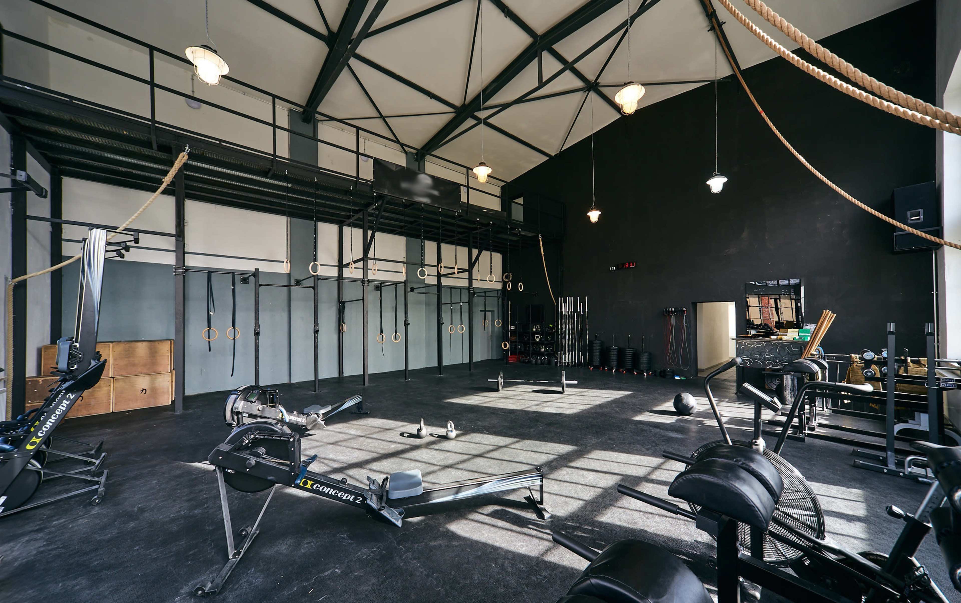 An industrial-style gym equipped with various fitness equipment, including rowing machines and weightlifting benches, under a high ceiling with exposed beams.