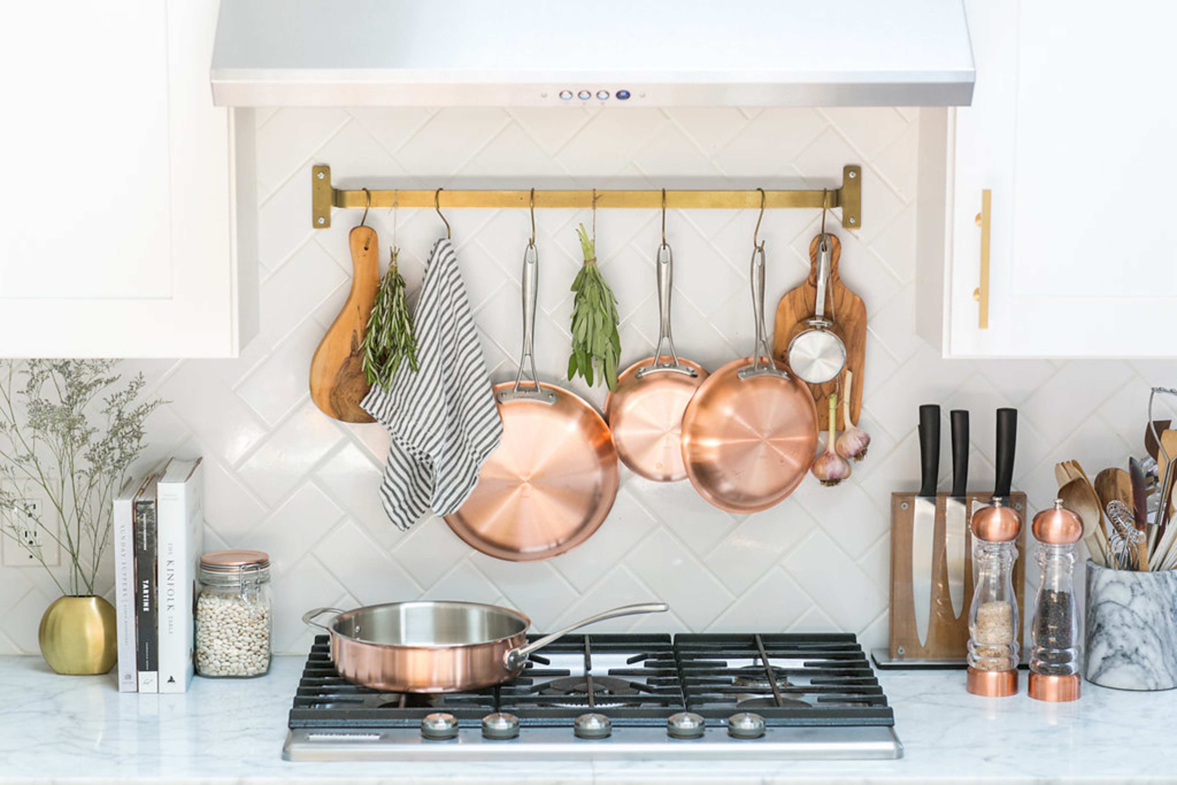 A modern kitchen with copper cookware hanging on a wall rack above a stovetop accompanied by various utensils and a spice rack.