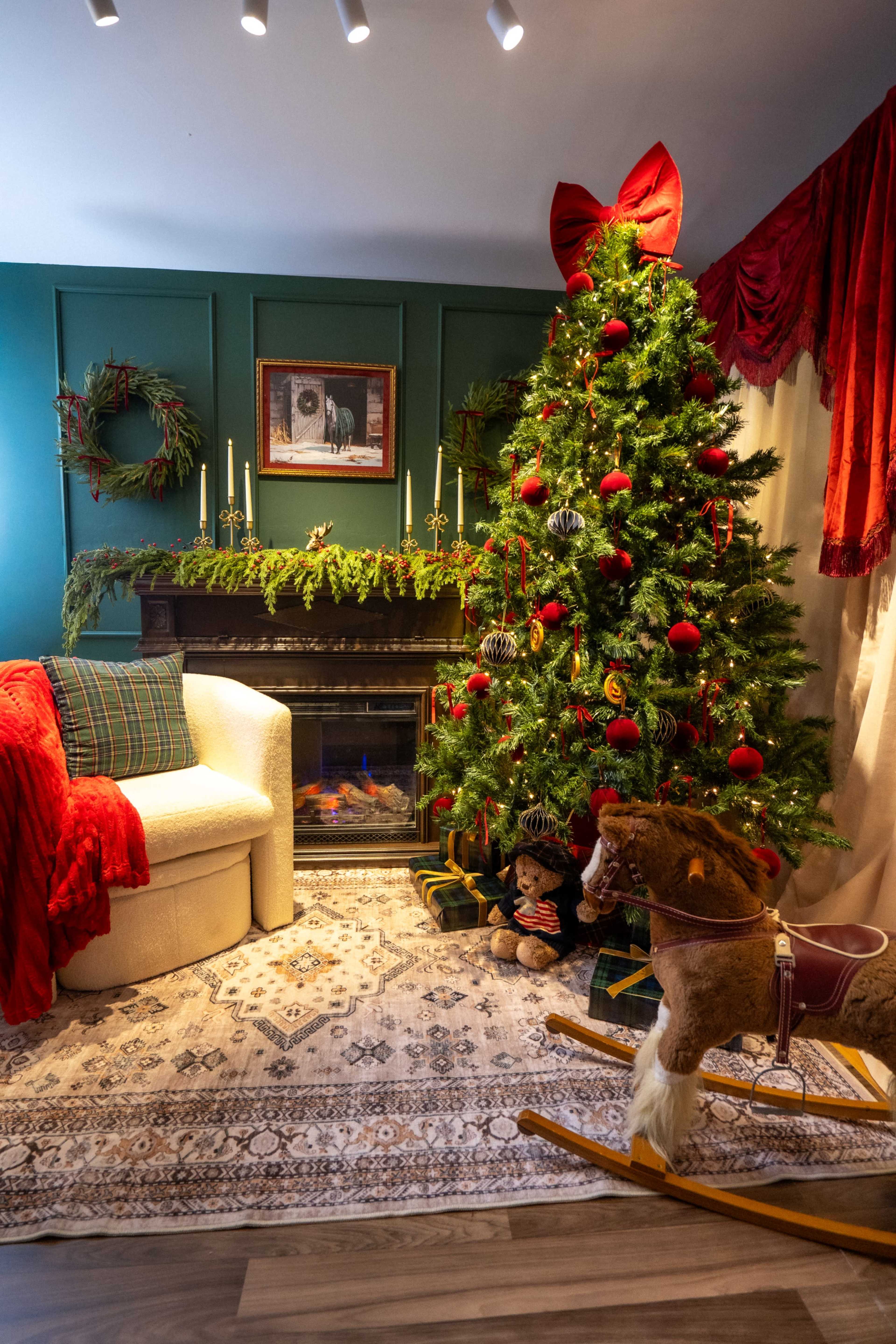 A cozy living room is adorned with a Christmas tree, a plush armchair, and festive decorations, including a fireplace and seasonal greenery.