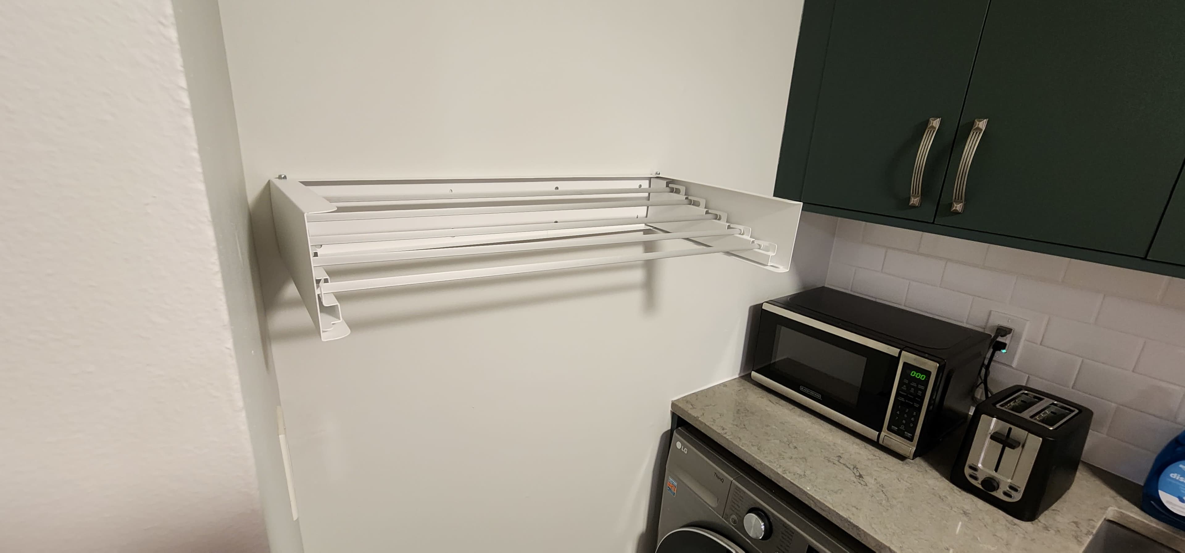 A white drying rack is mounted on a wall next to a countertop with a microwave and a washing machine.