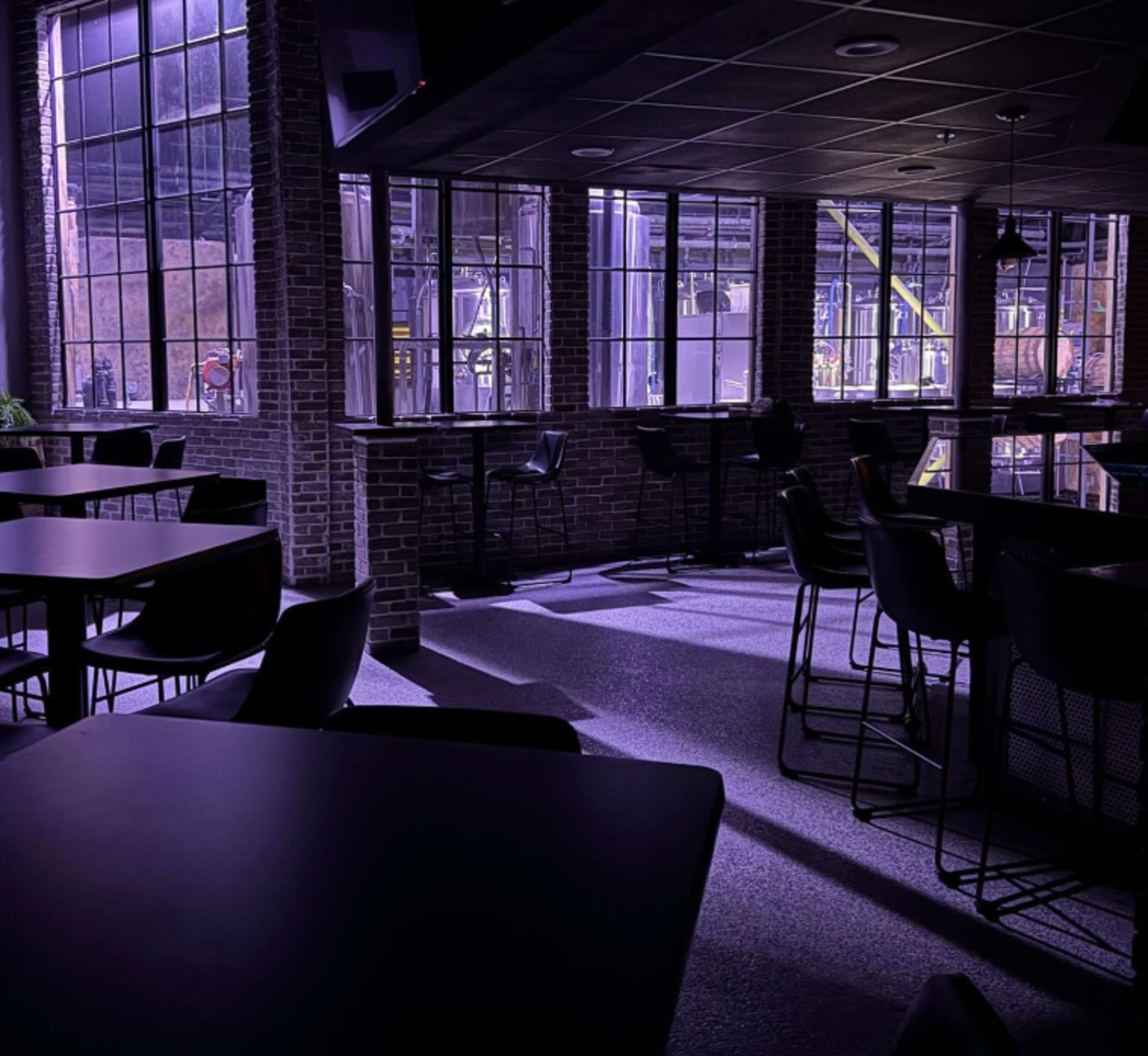 The image shows an empty, dimly lit interior of a modern café with large windows and industrial-style furnishings.