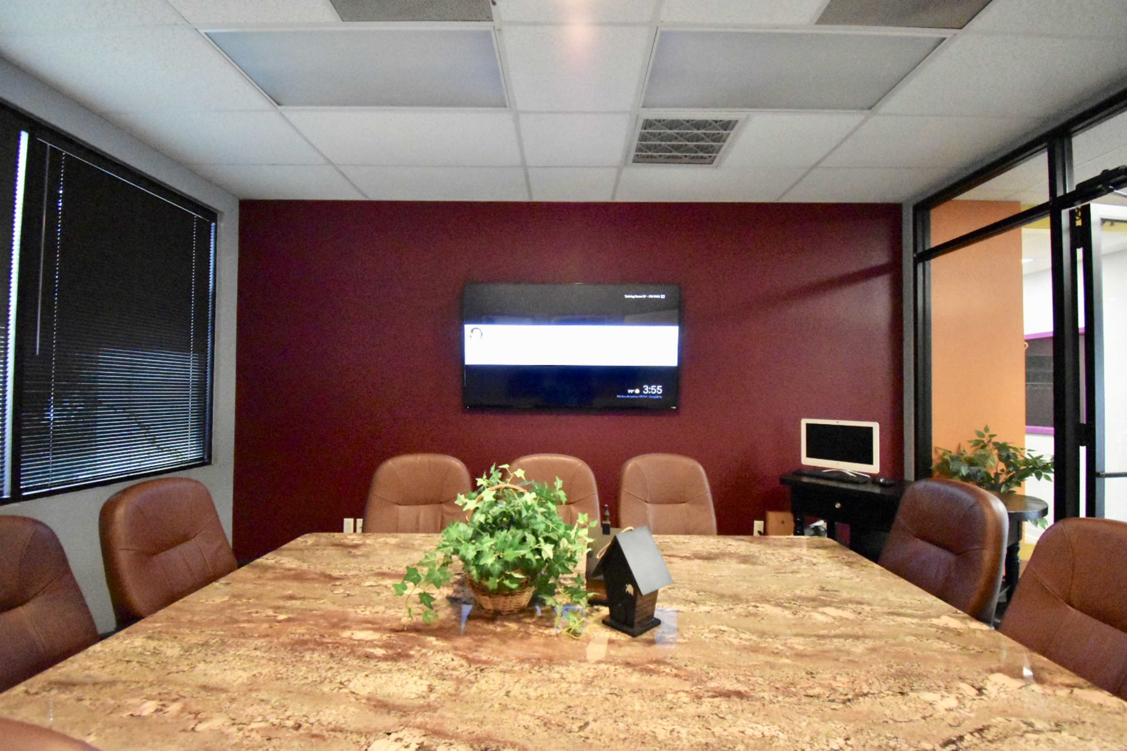 A conference room features a large marble table, leather chairs, and a wall-mounted television.