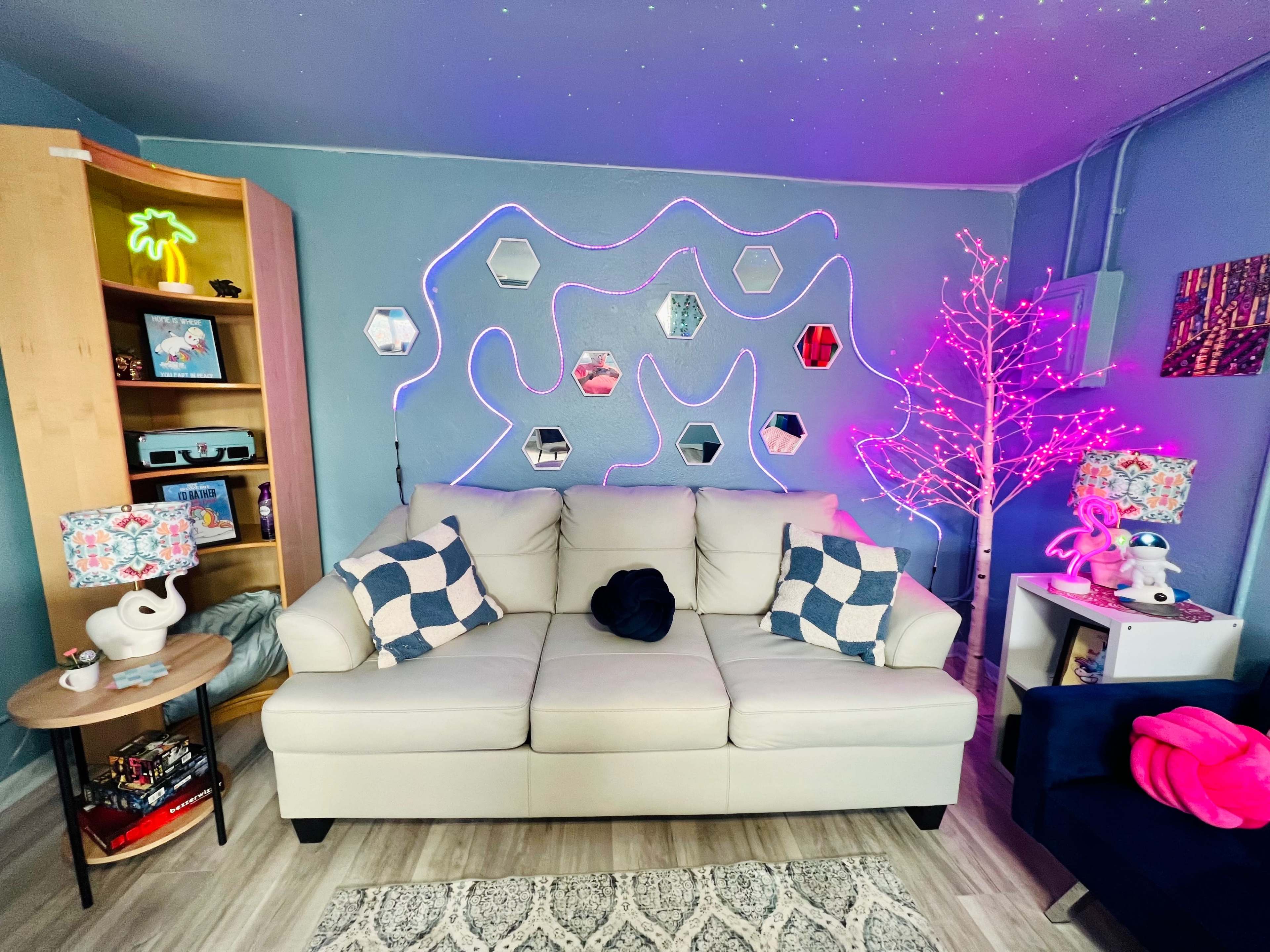 A light-colored sofa is centered in a room decorated with colorful accents, a glowing tree, and wall-mounted mirrors.