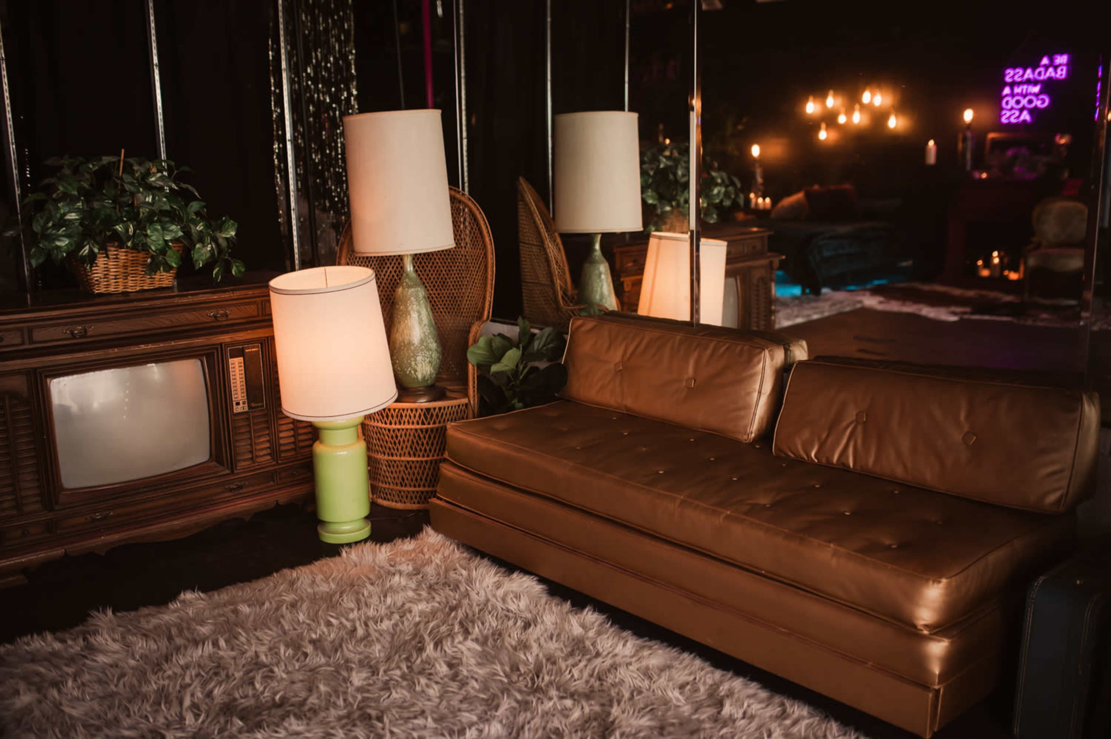 A vintage living room setting with a brown leather couch, a retro television set, a green and white lamp, and plush white carpeting.