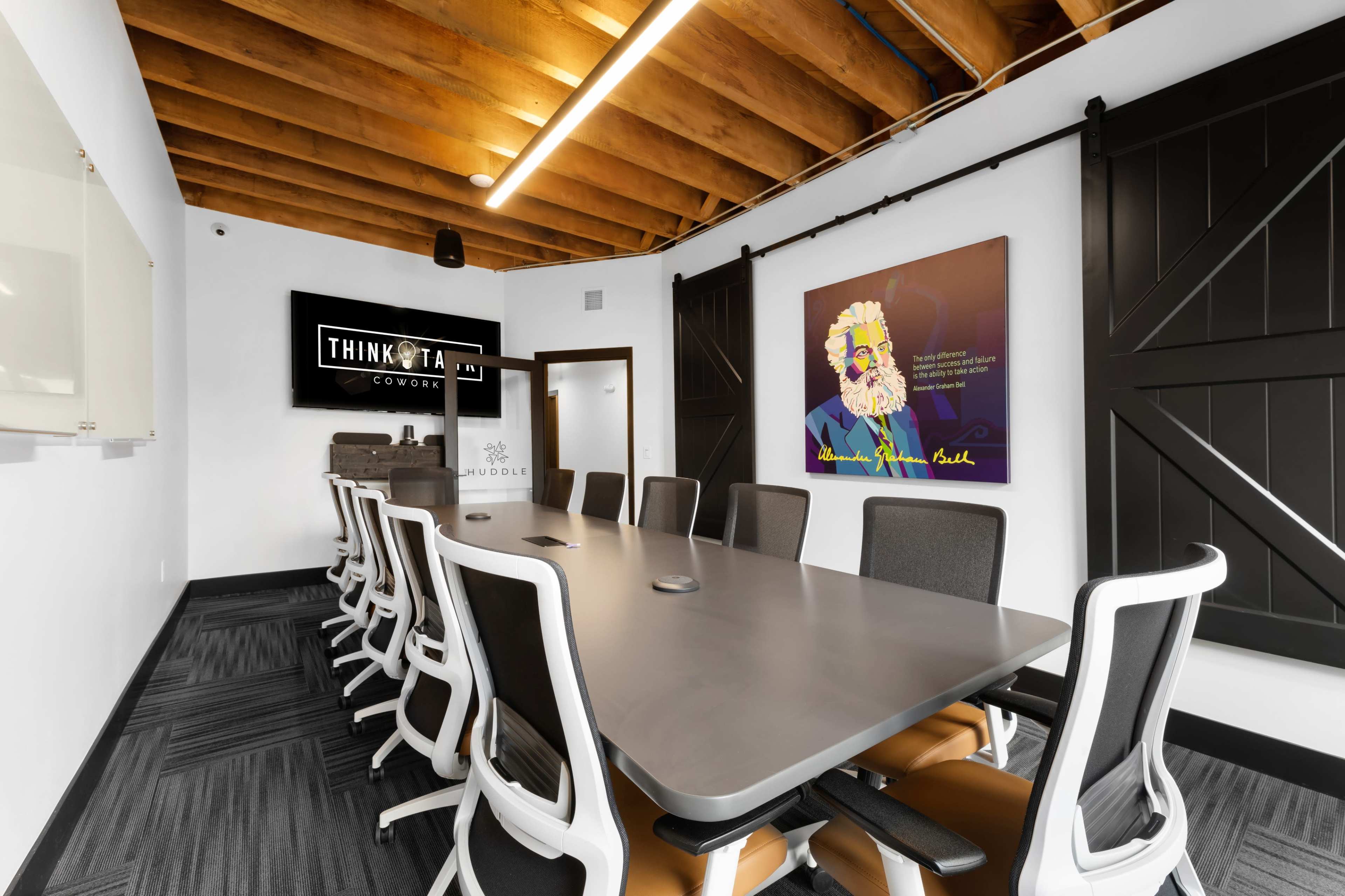 A modern conference room features a long table with ergonomic chairs, a large screen for presentations, and a colorful artwork on the wall.