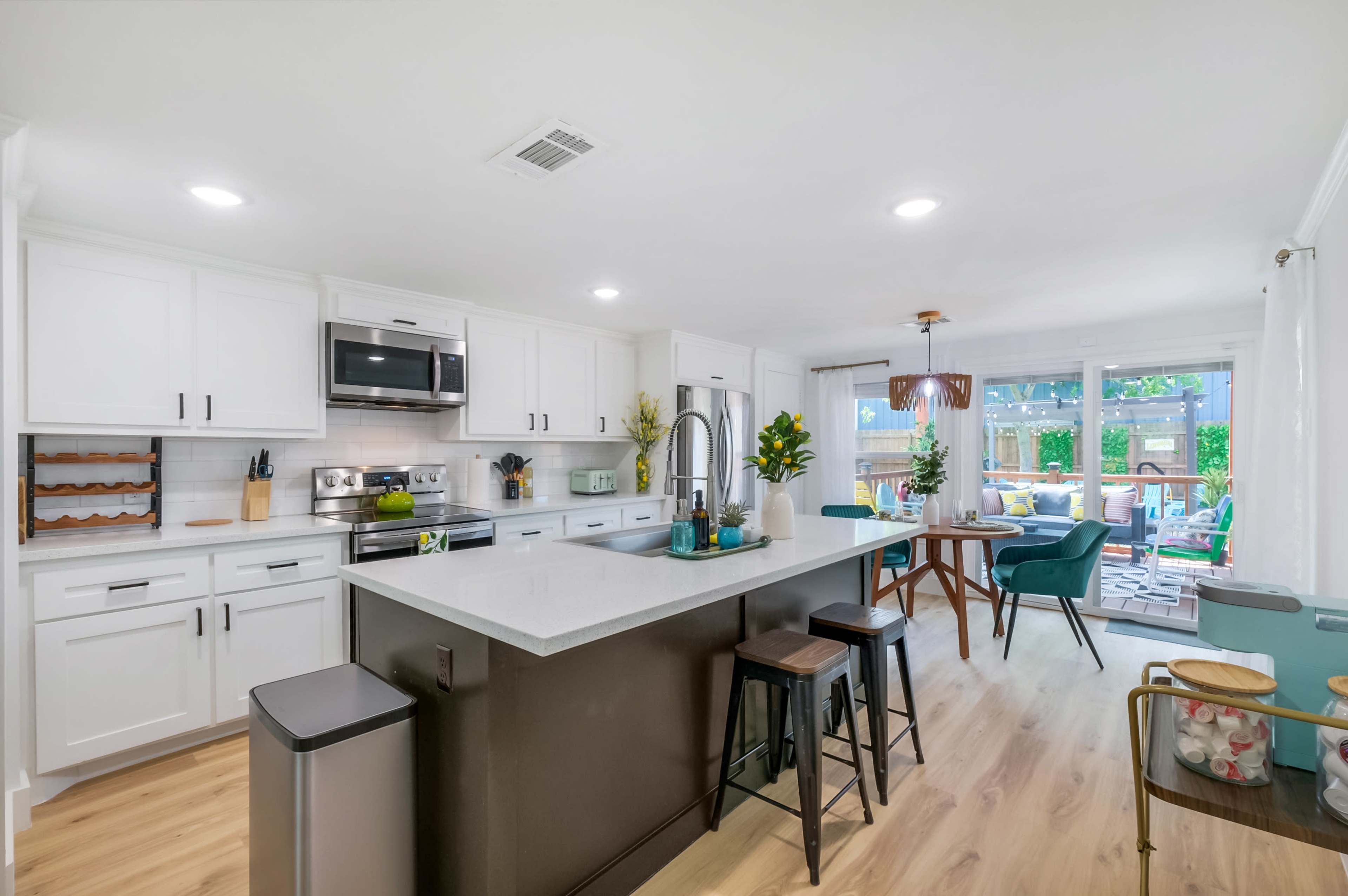 The kitchen features white cabinetry, stainless steel appliances, and a central island with seating, alongside a dining area with a view of the outdoor space.