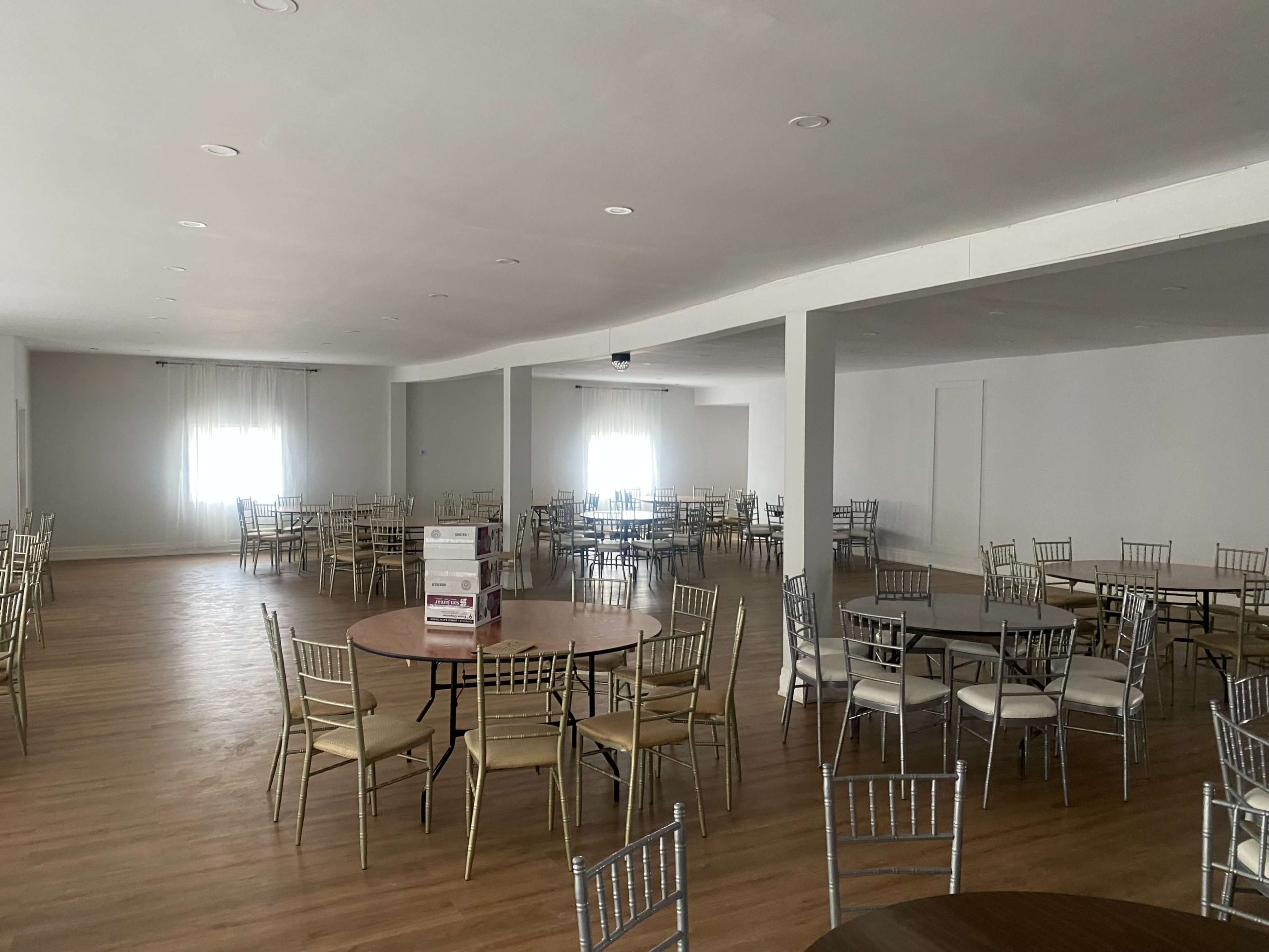 The image shows a large, empty banquet hall with several round tables and chairs arranged throughout the space.