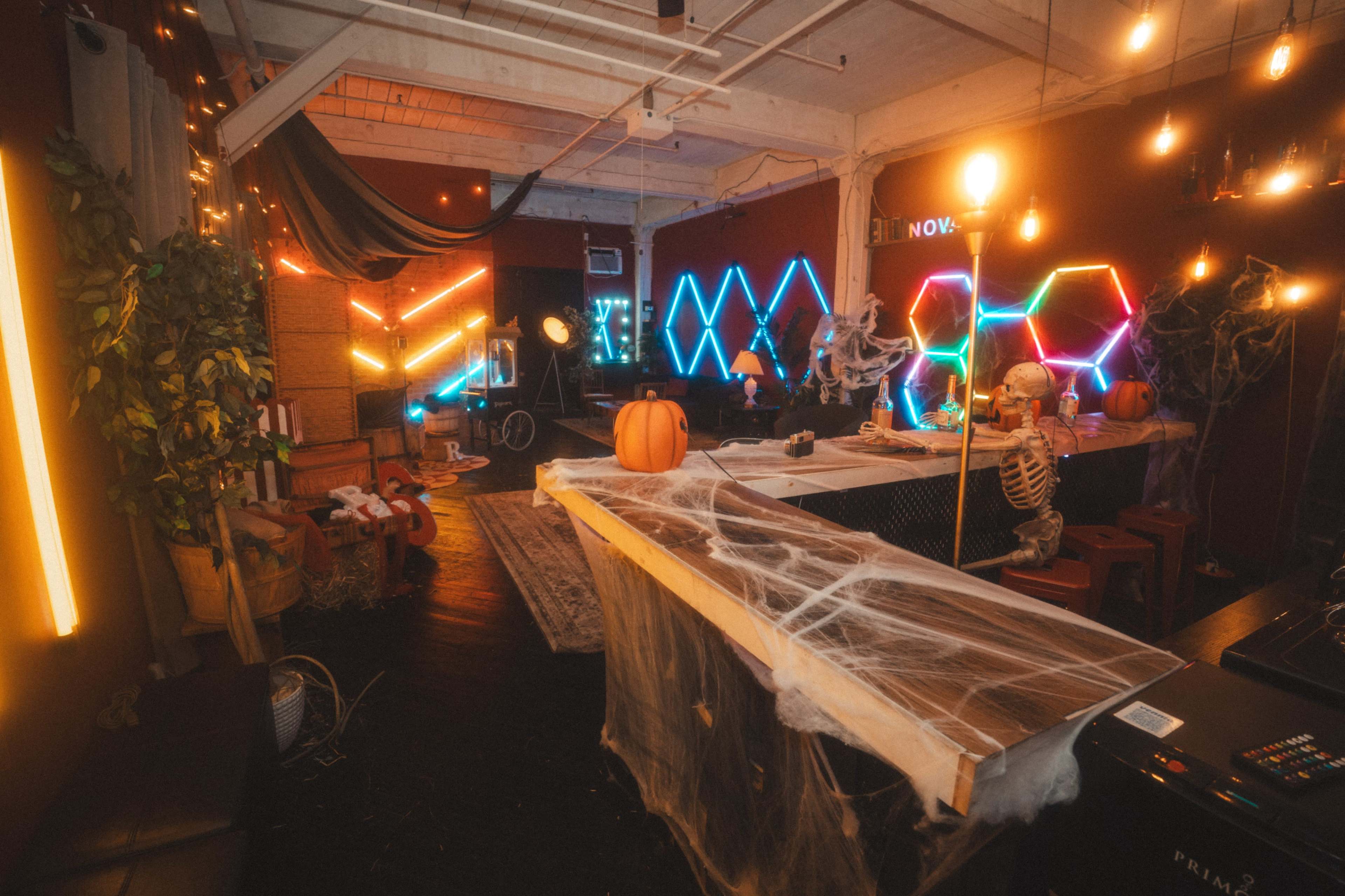 The image depicts a creatively decorated indoor space featuring neon lights, Halloween decorations, and a skeleton, with a large wooden counter at the forefront.