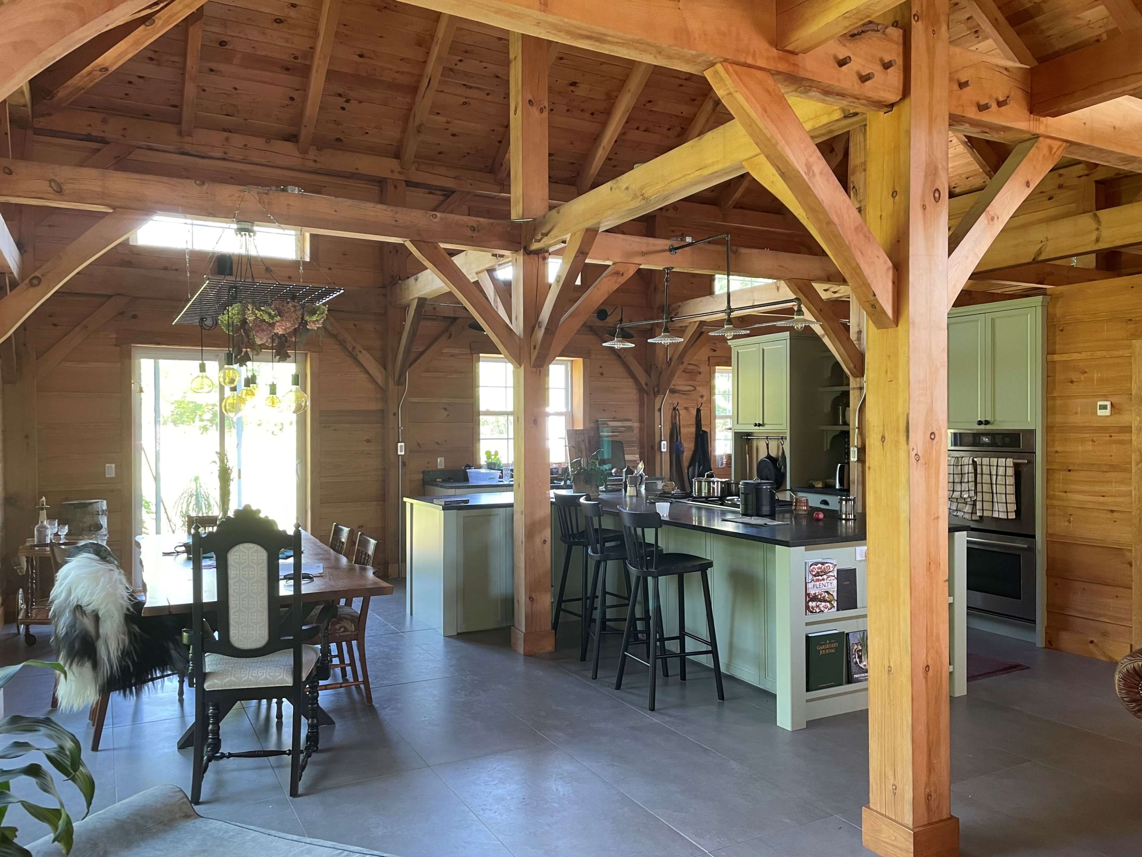A spacious wooden kitchen and dining area featuring a large table, bar stools, and an open layout with exposed beams.