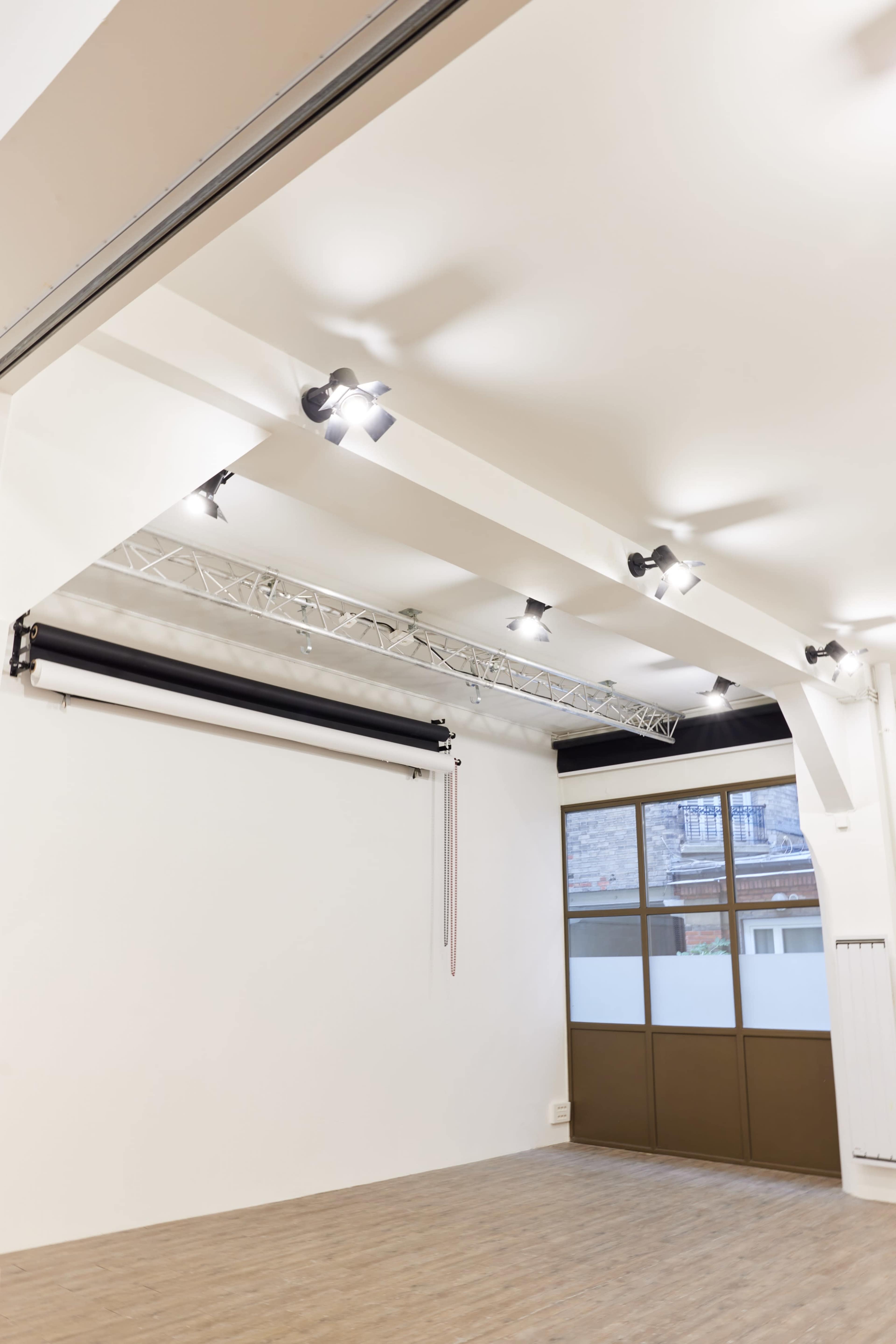 The image shows a spacious, well-lit studio with ceiling lights and a large window.