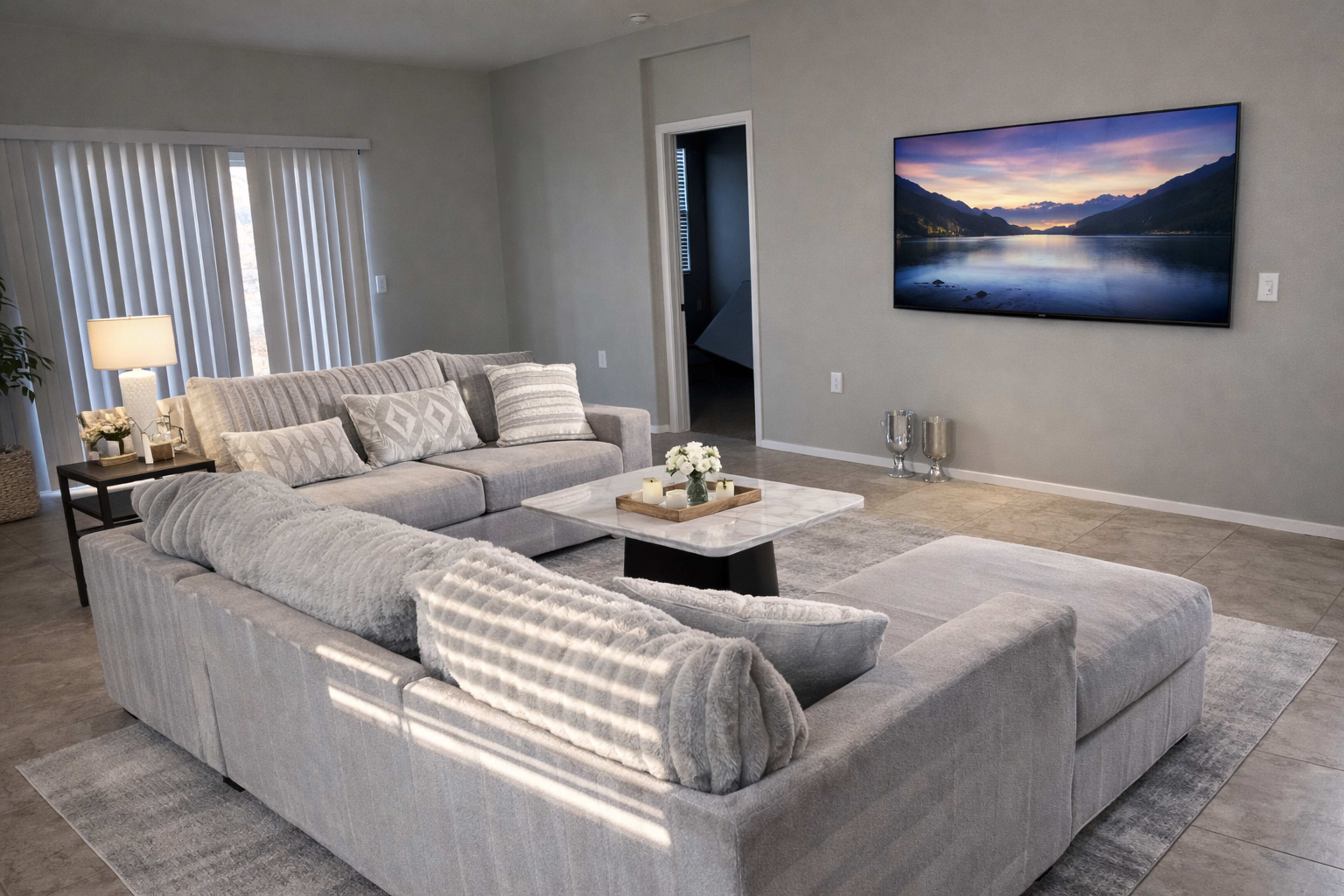 The spacious living room features two large gray sofas facing a wall-mounted television, with a coffee table adorned with decorative items in the center.