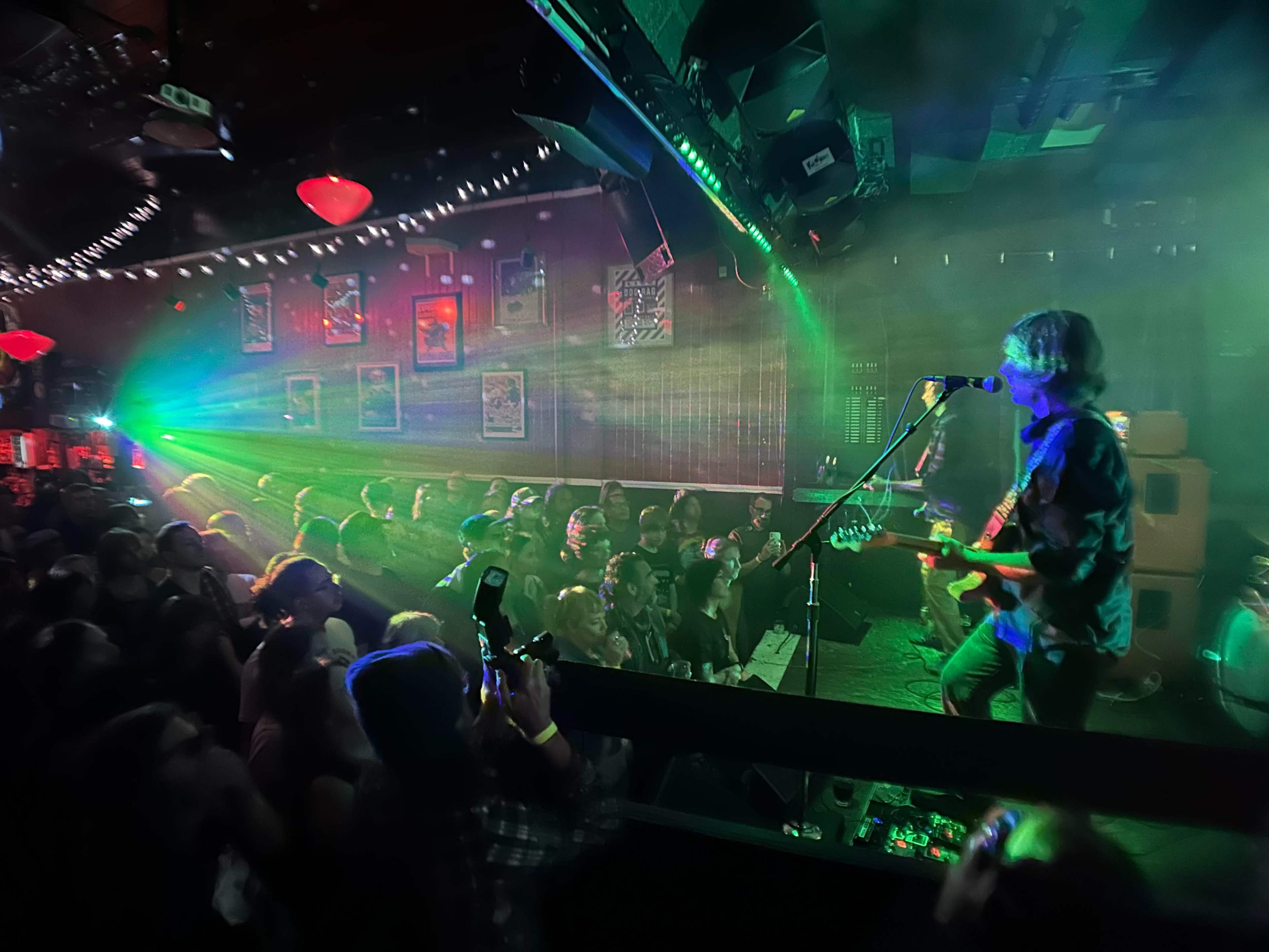 A musician plays guitar on stage while colorful lights illuminate the crowd in a lively music venue.