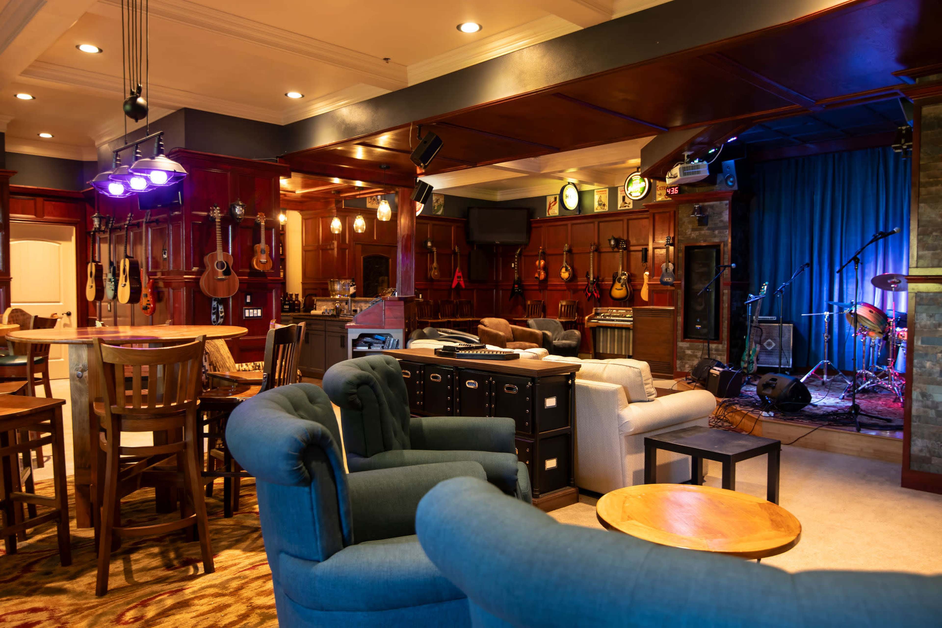 A cozy music lounge featuring wooden decor, a stage with musical instruments, and comfortable seating arrangements.