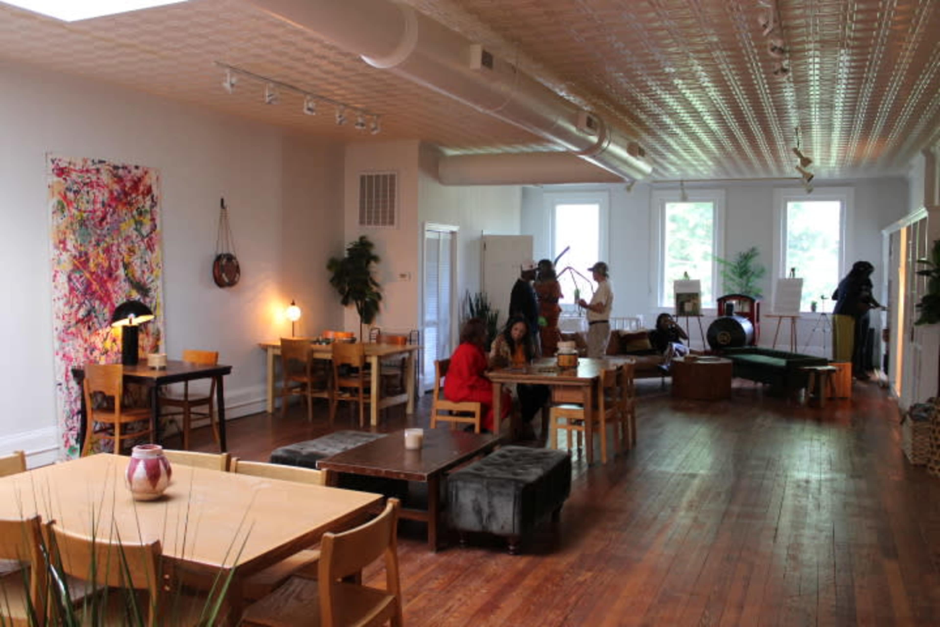 A spacious café with wooden floors and various seating arrangements, including tables and couches, accompanied by art pieces and plants.