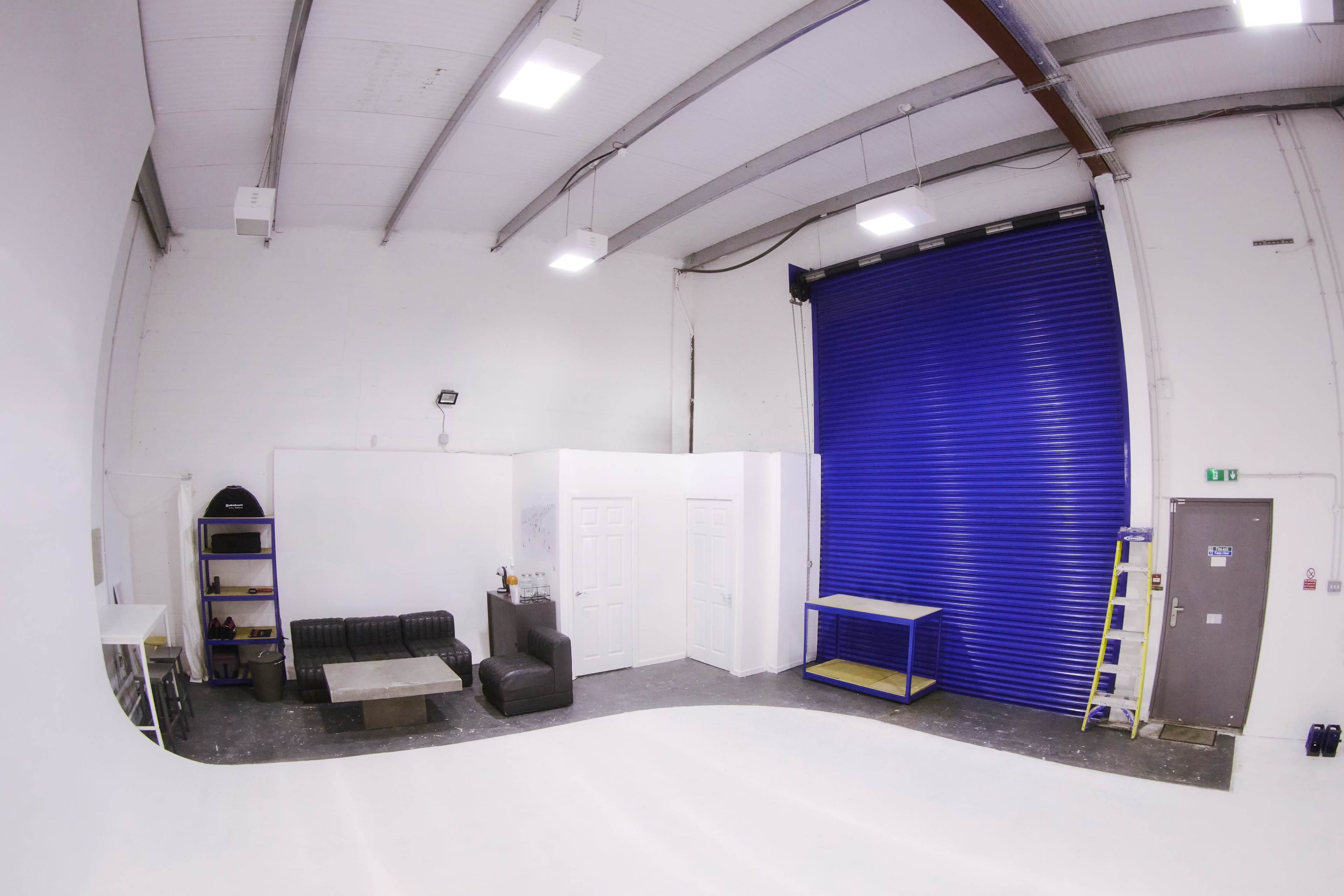 A spacious studio with white walls, a black couch, a coffee table, and a large blue roll-up door.