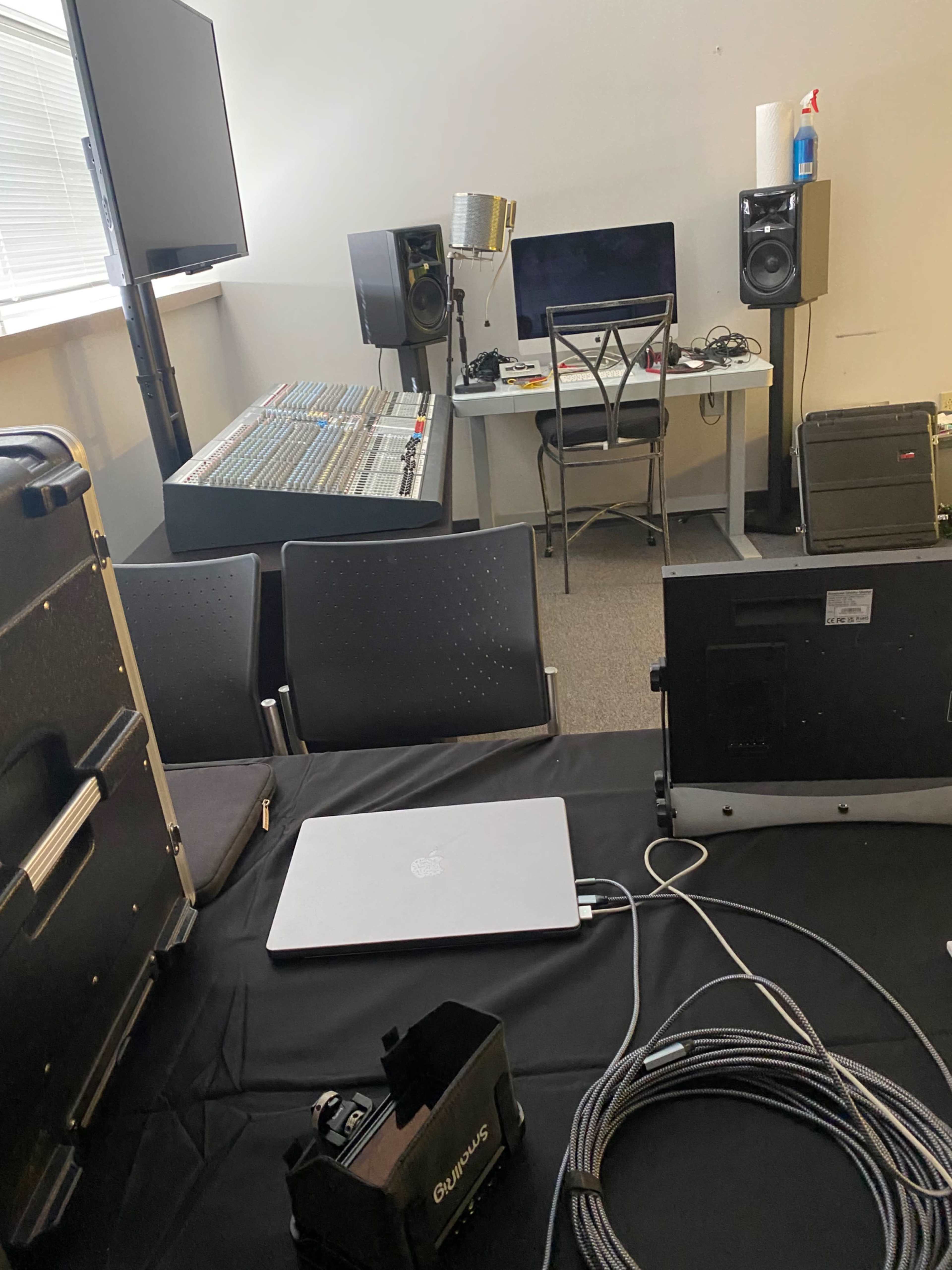 The image shows a music production studio with audio equipment, a computer setup, and monitoring speakers.