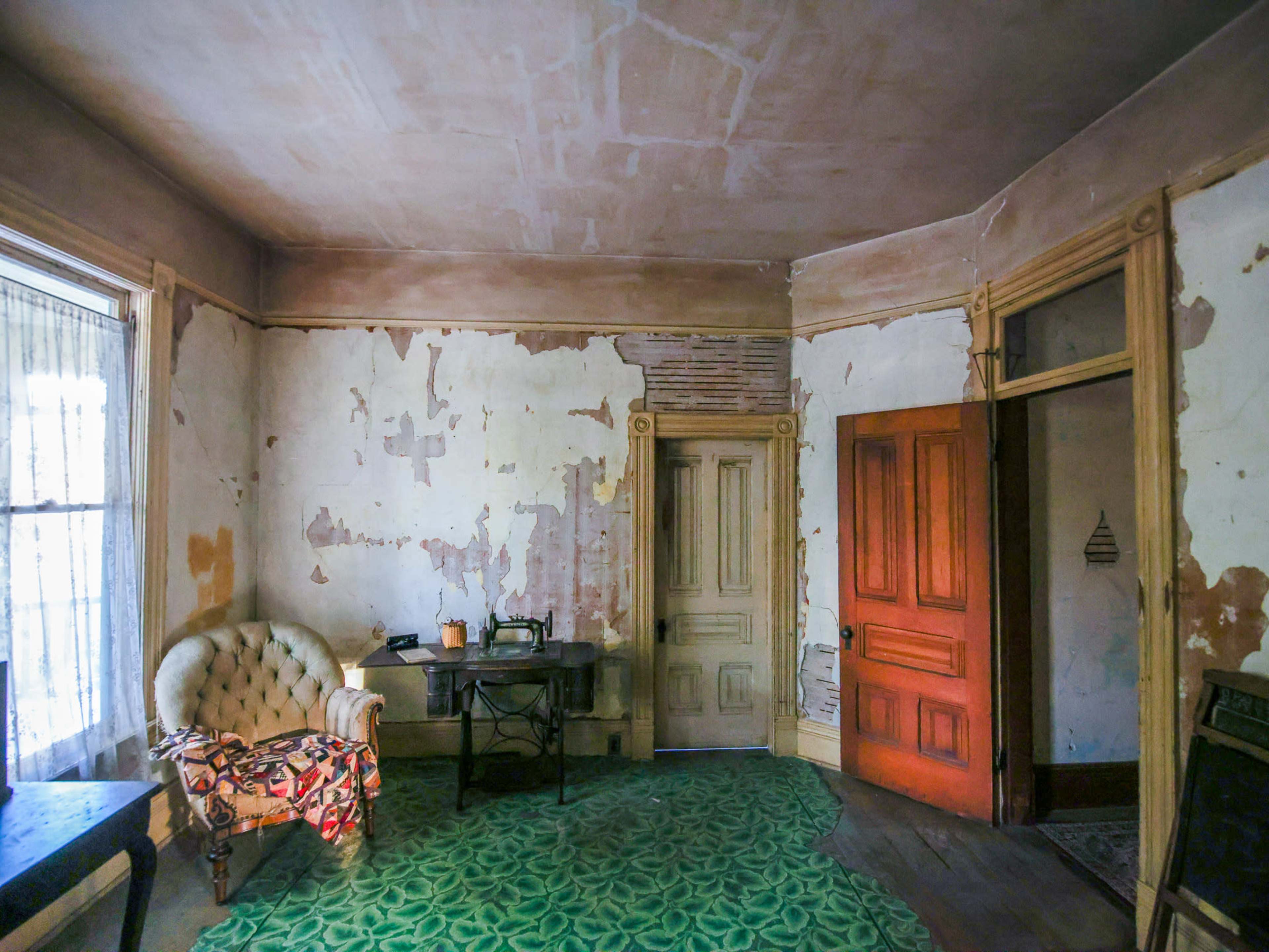 The image depicts a dilapidated room with peeling paint on the walls, a vintage armchair, a wooden table, and a closed door with a contrasting orange hue.