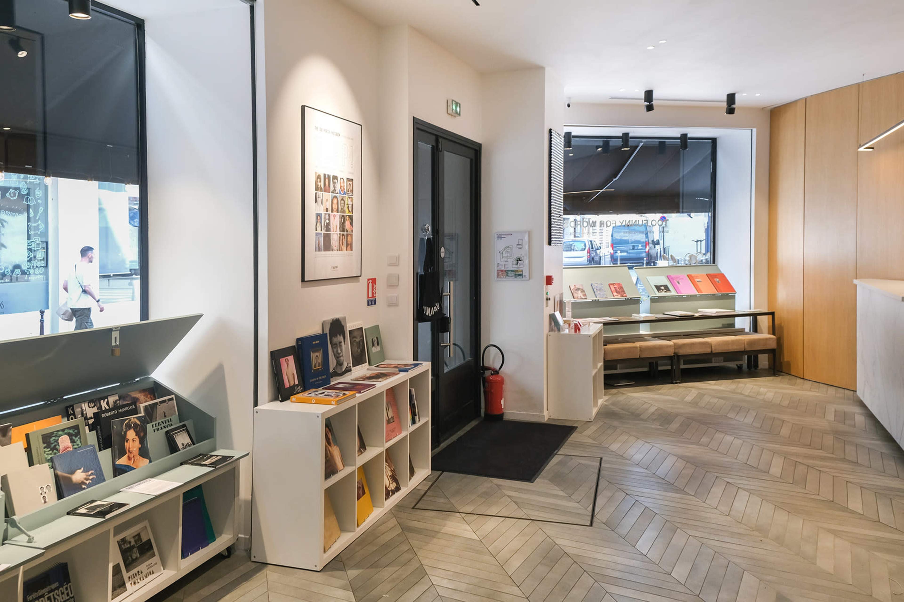 The image shows a modern interior of a space featuring shelves of magazines, seating, and a large glass window.