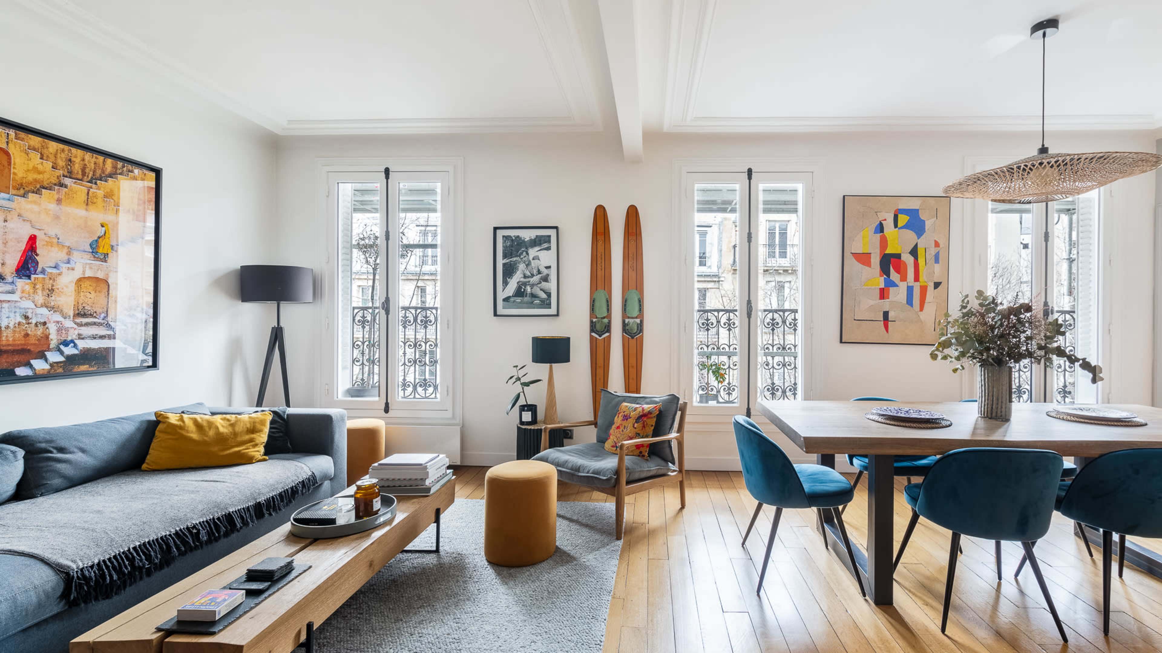 A modern living and dining area features a gray sofa, wooden dining table, and two vintage wooden skis displayed on the wall.