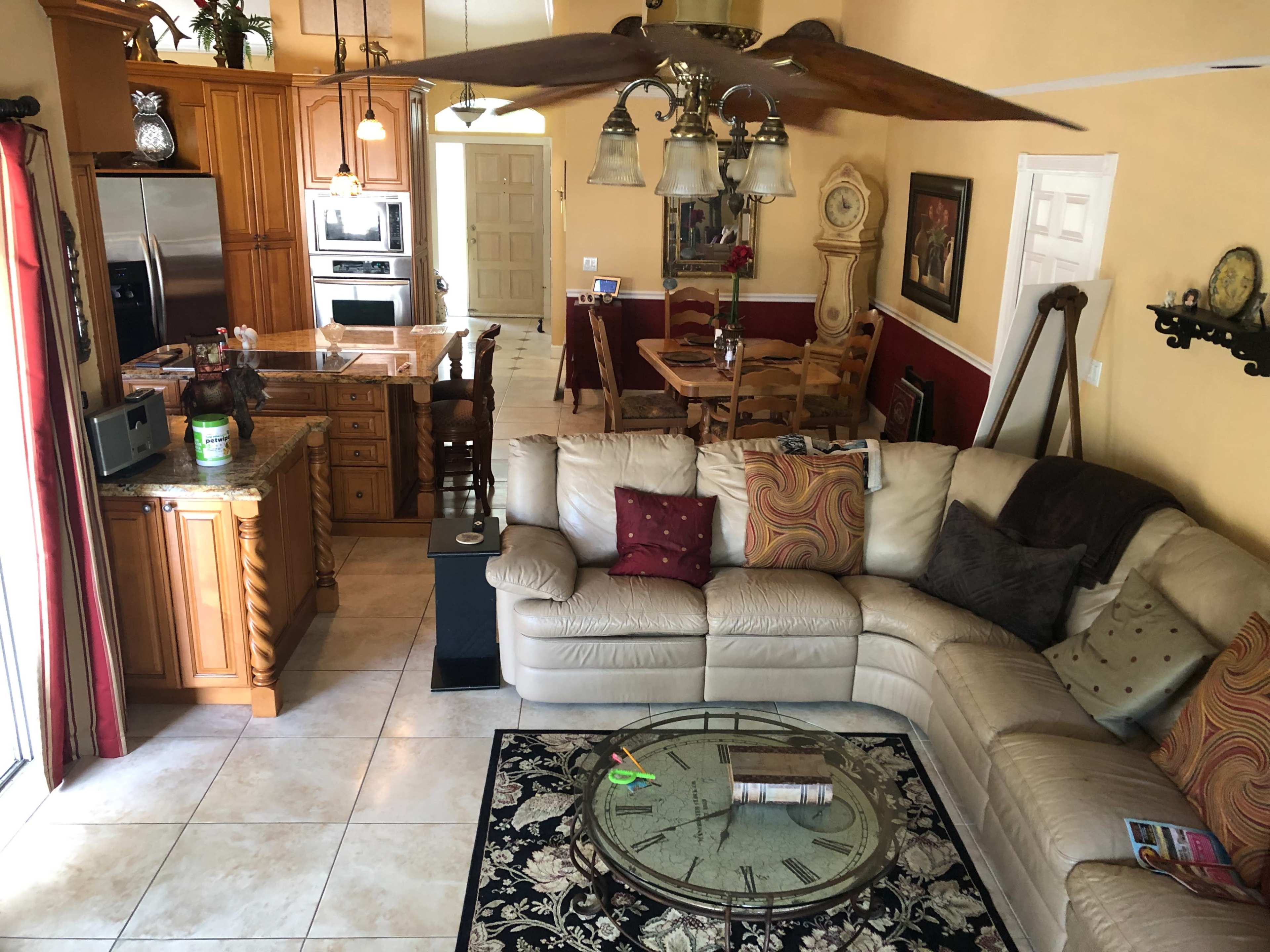 A spacious living area featuring a beige sectional sofa, a round coffee table with magazines, and a dining area with a wooden table and chairs against a backdrop of warm-colored walls.