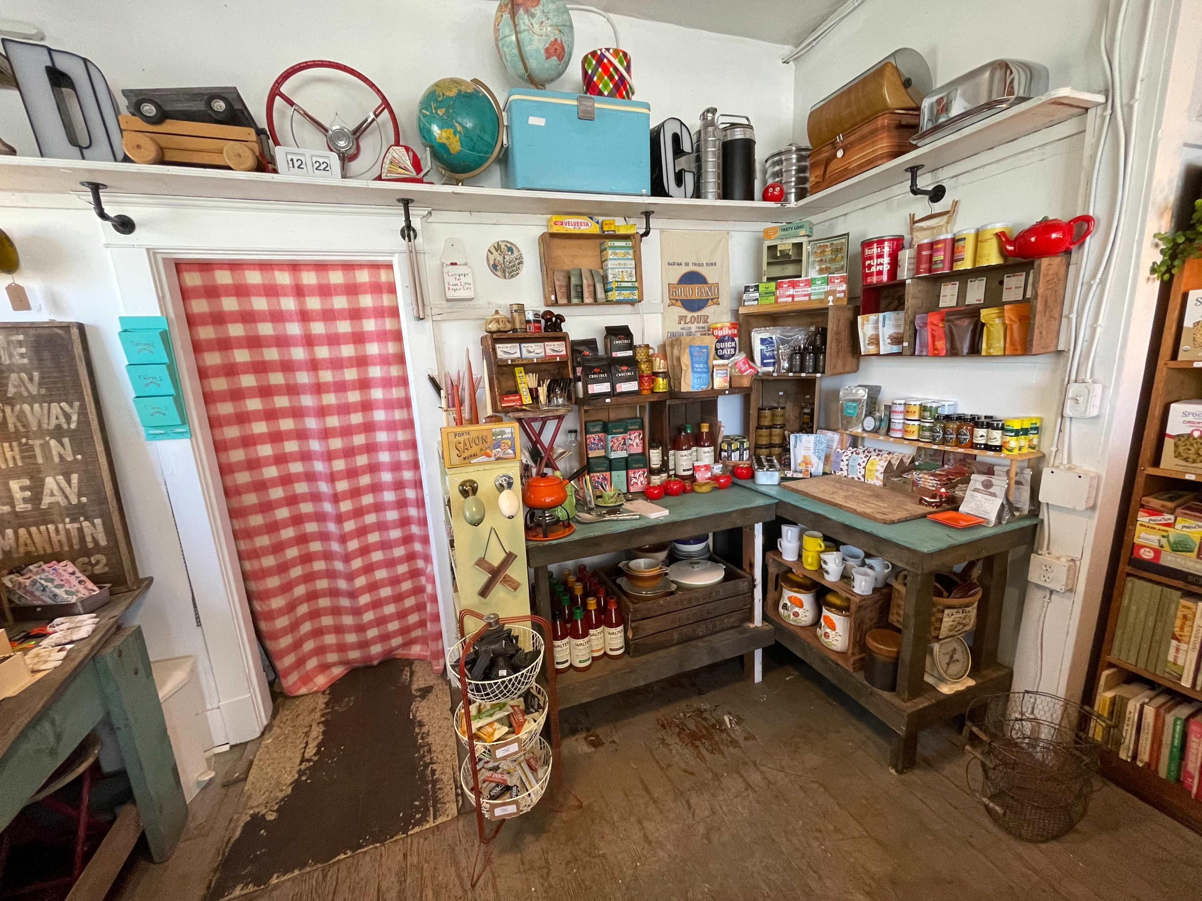 A vintage-style kitchen pantry filled with an assortment of canned goods, jars, and kitchen tools, arranged on wooden shelves.