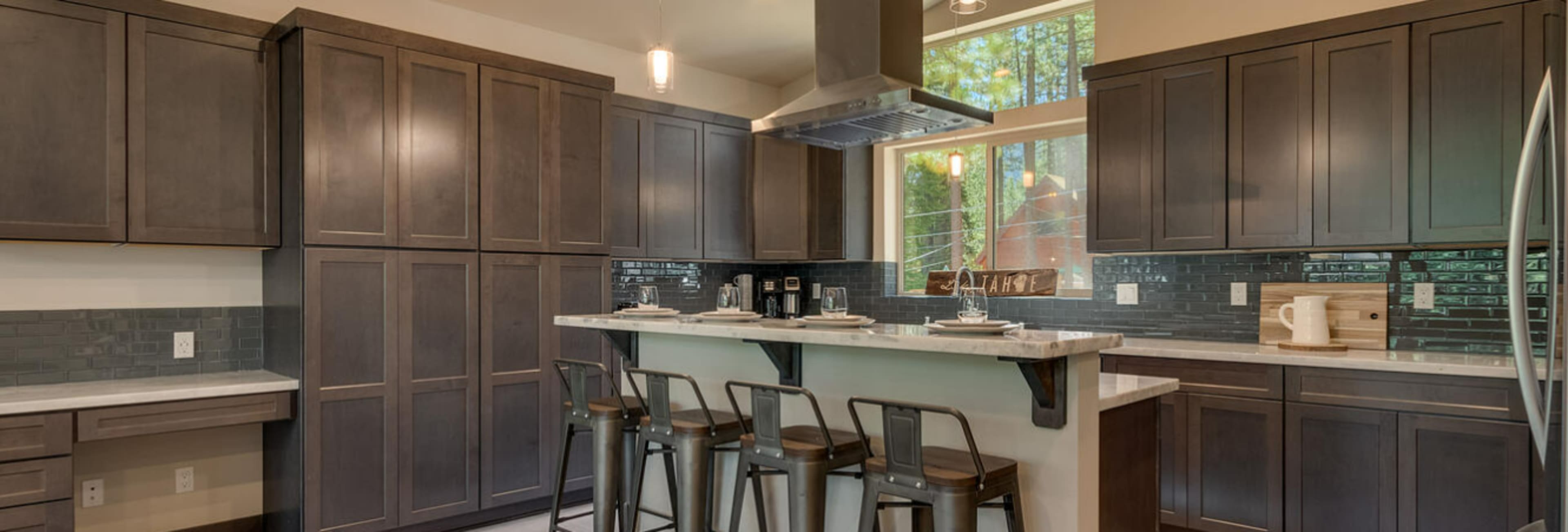 A modern kitchen with dark cabinetry, a central island with bar stools, and a large window overlooking greenery.