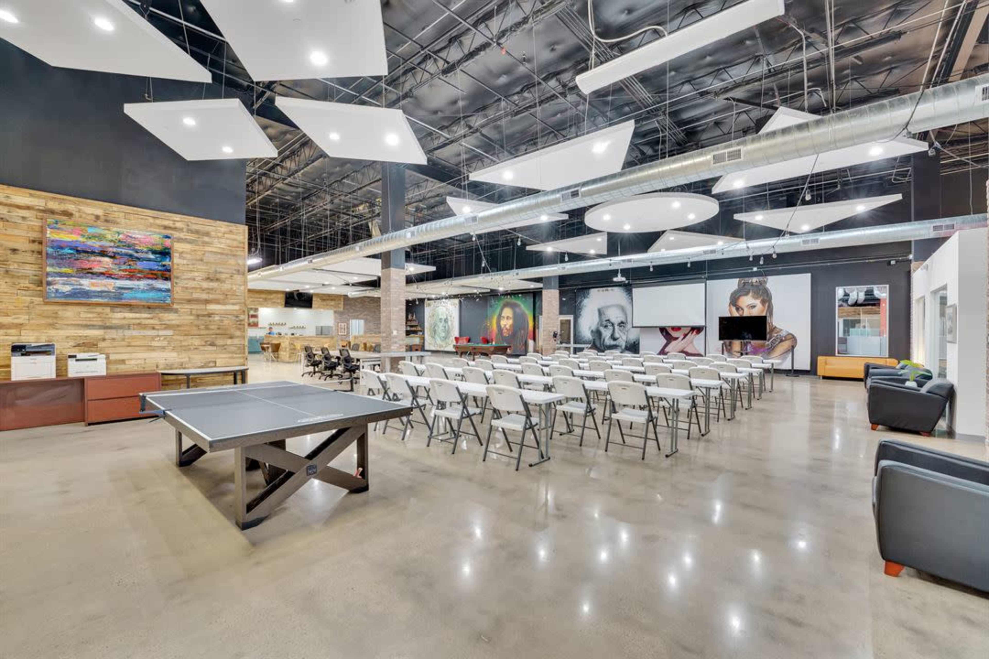 A spacious indoor venue with folding chairs arranged in rows, a ping pong table, and large wall art in a well-lit environment.