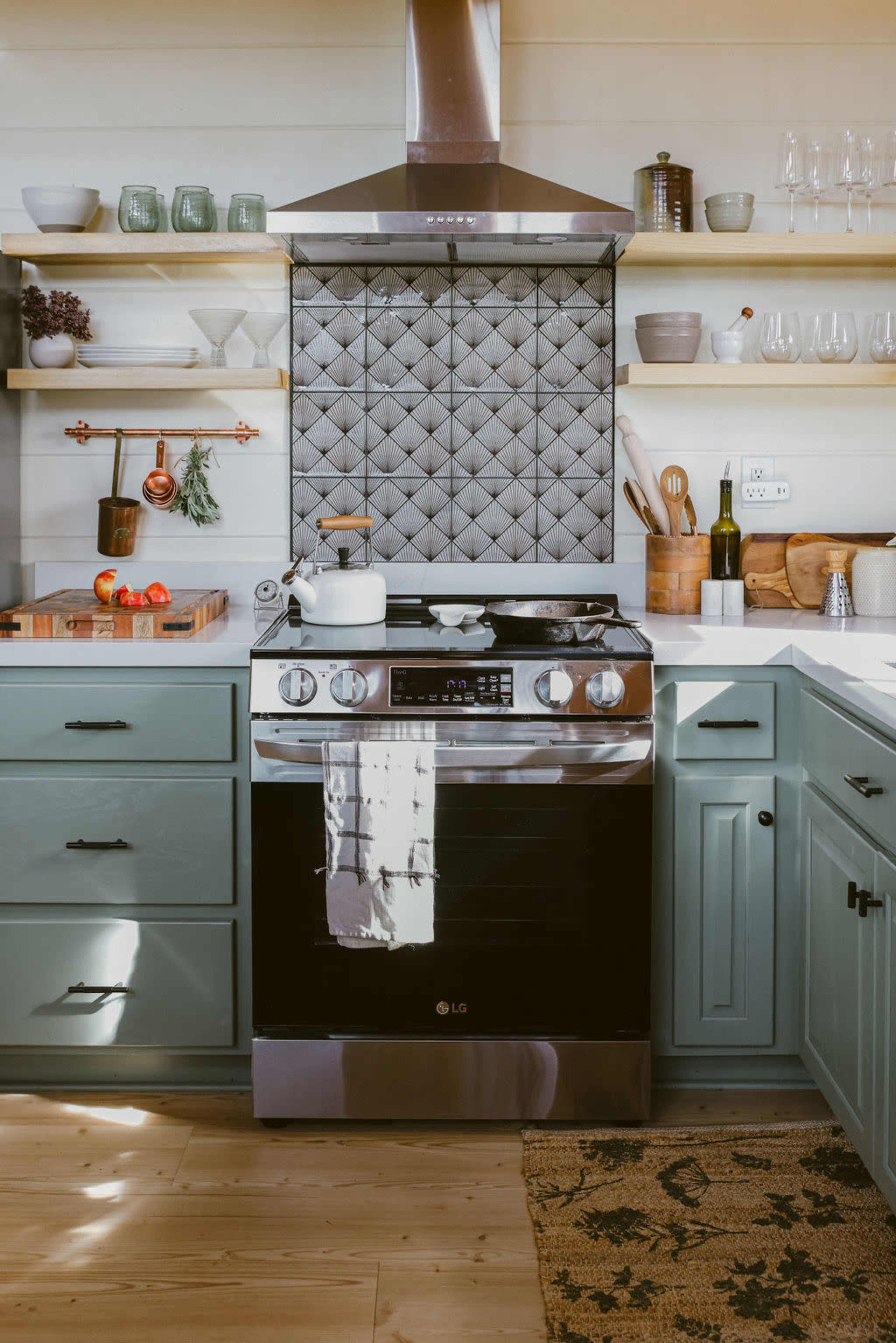 A modern kitchen with teal cabinets, a stainless steel oven, and a decorative tiled backsplash.