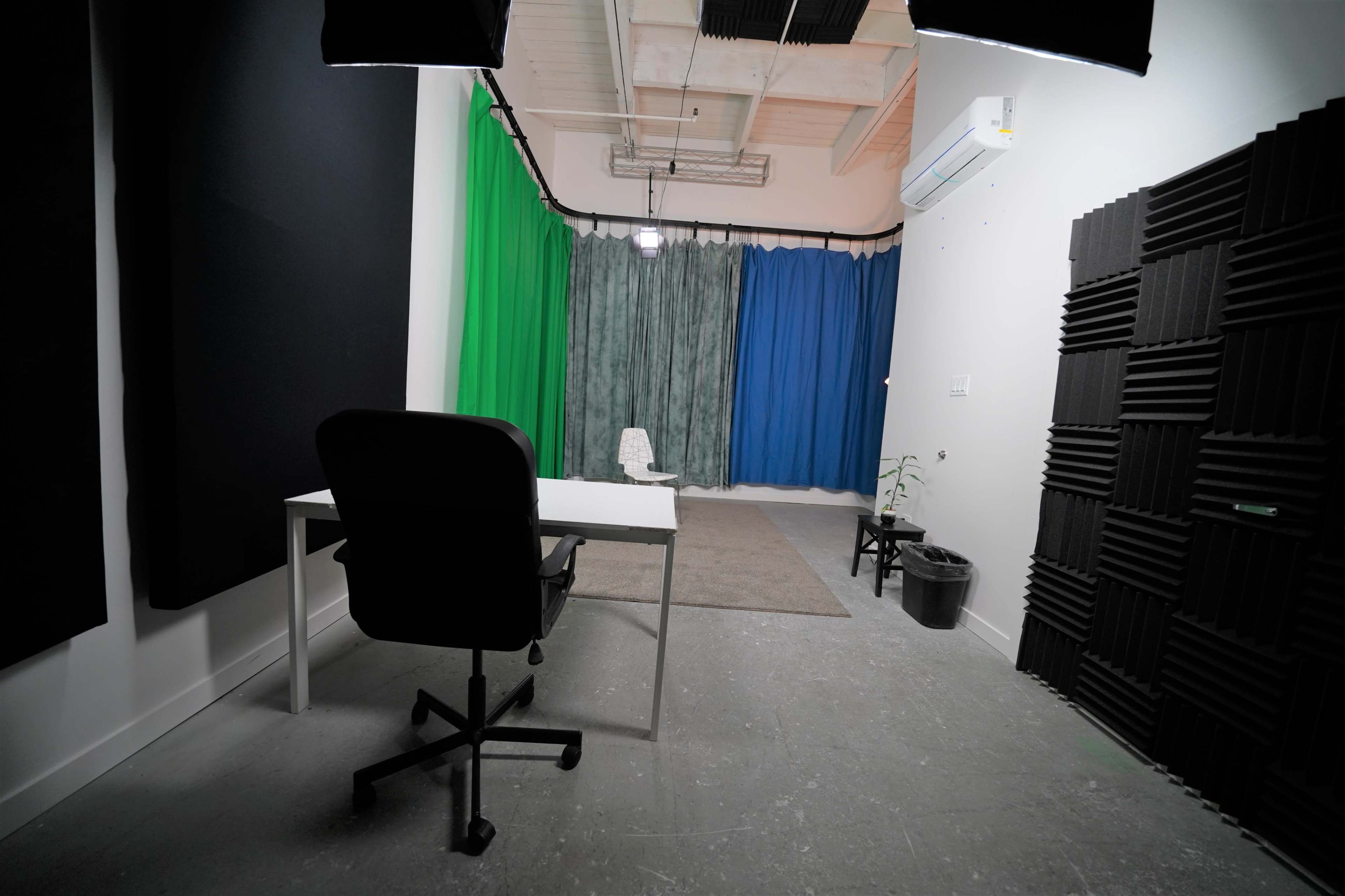 A studio space with a desk and chair in front, surrounded by colored curtains and soundproofing panels.