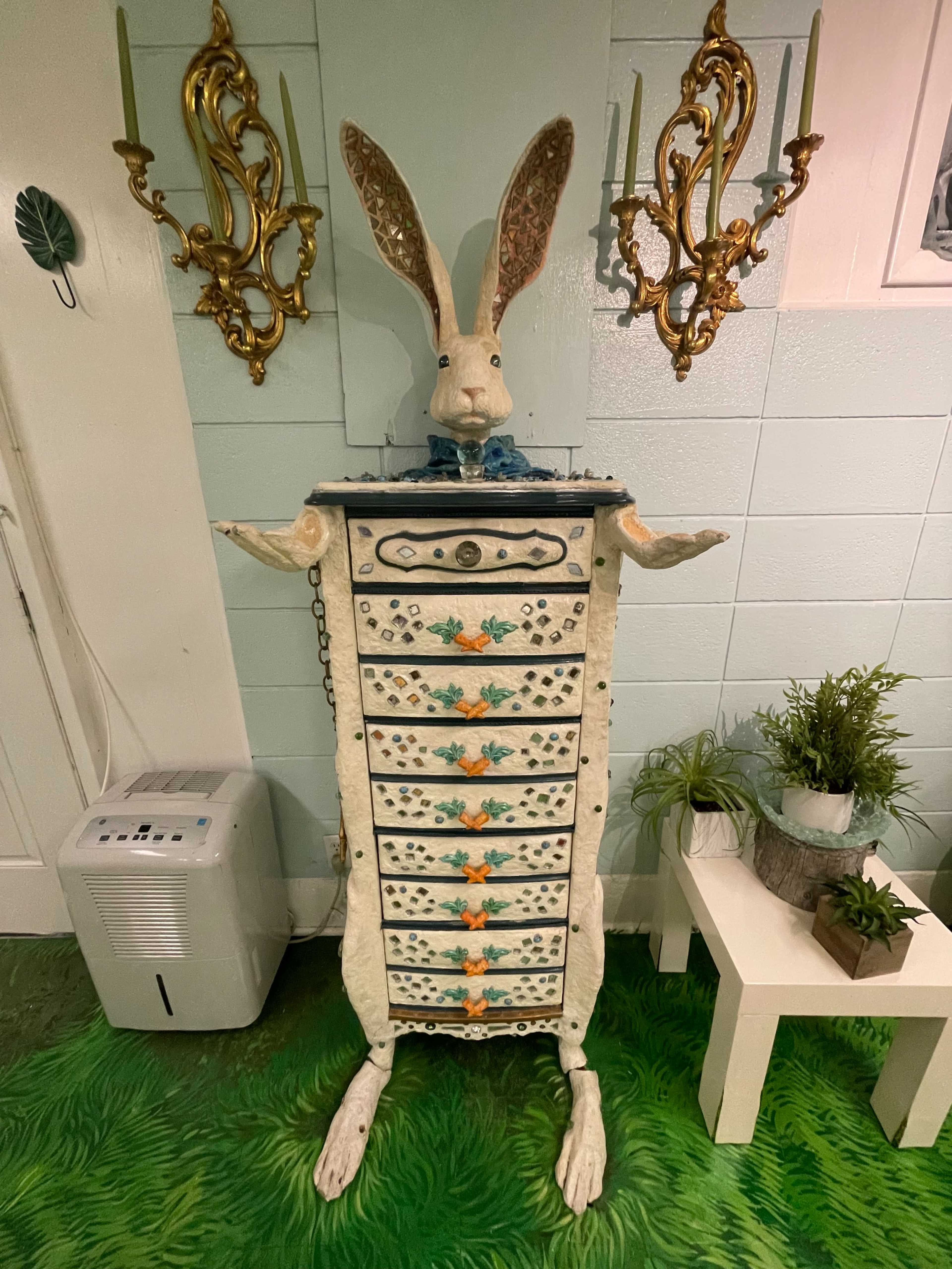 A whimsical cabinet in the shape of a rabbit stands against a wall, featuring ornate drawer handles and decorative patterns.