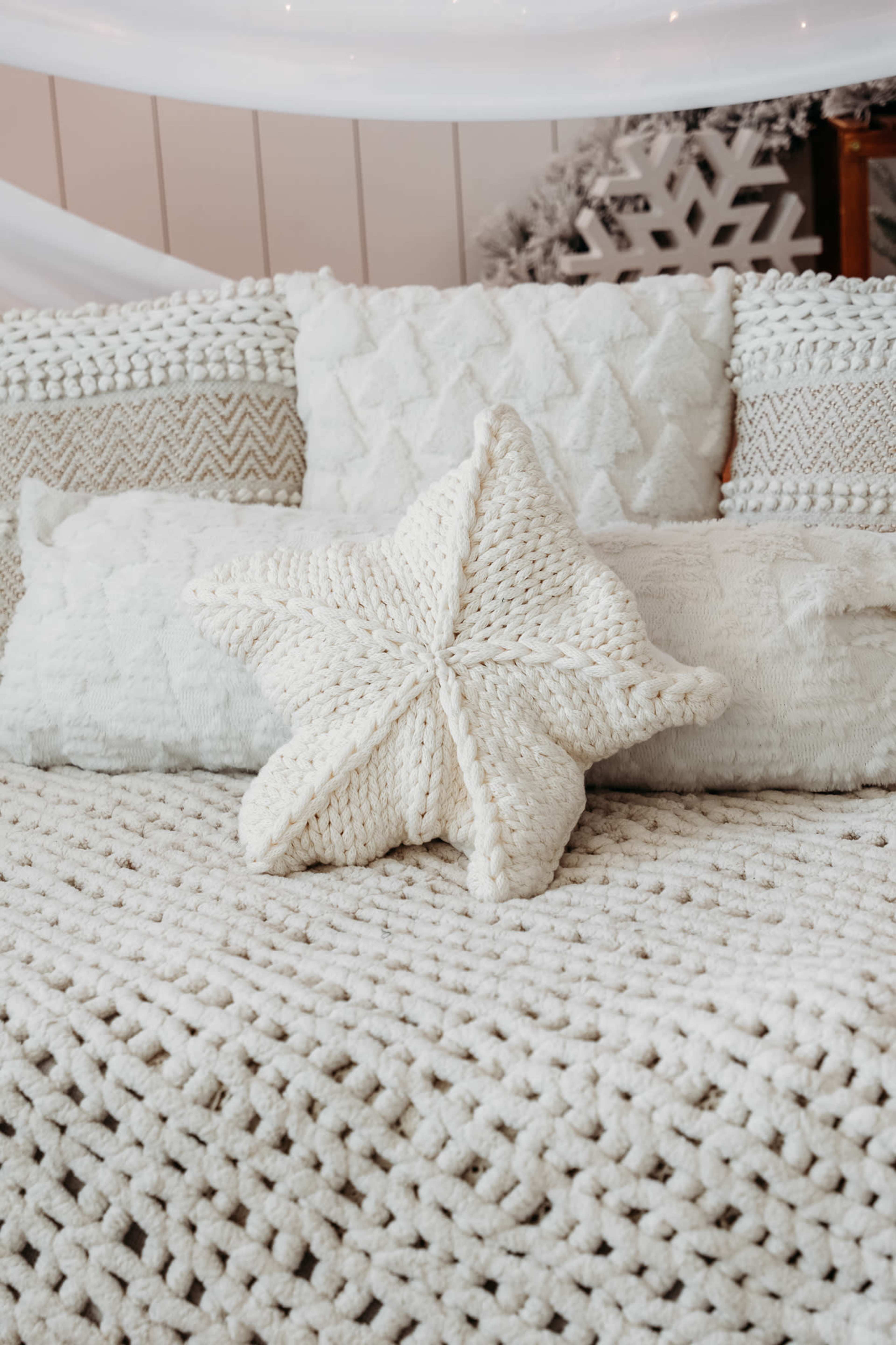 A cozy couch is adorned with textured white pillows and a star-shaped knitted throw pillow, set against a softly lit background.