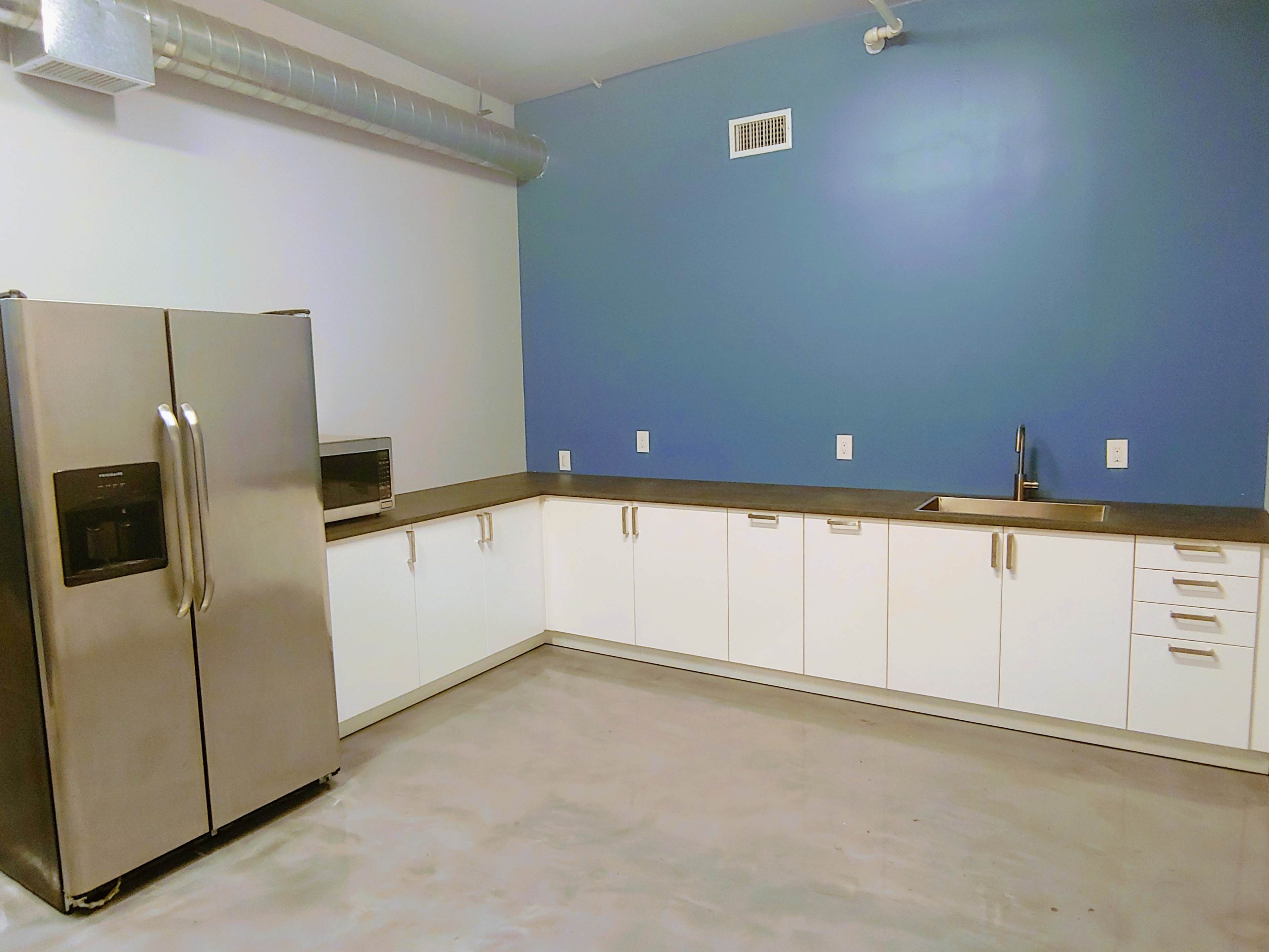 The image shows a modern kitchen with stainless steel appliances, white cabinetry, a blue accent wall, and a concrete floor.
