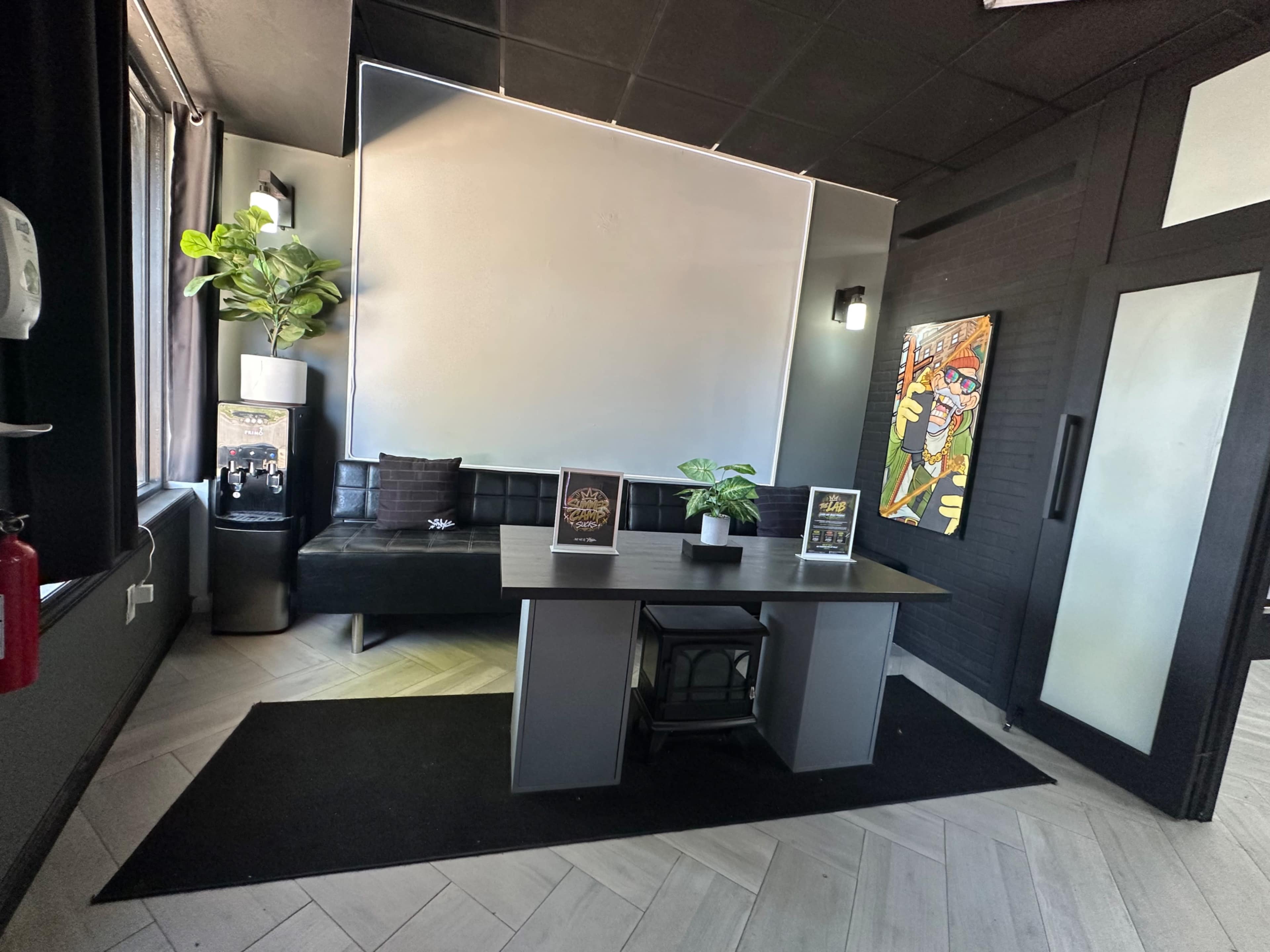 The image shows a modern waiting area featuring a black sofa, a table with plants, and artwork on the walls.
