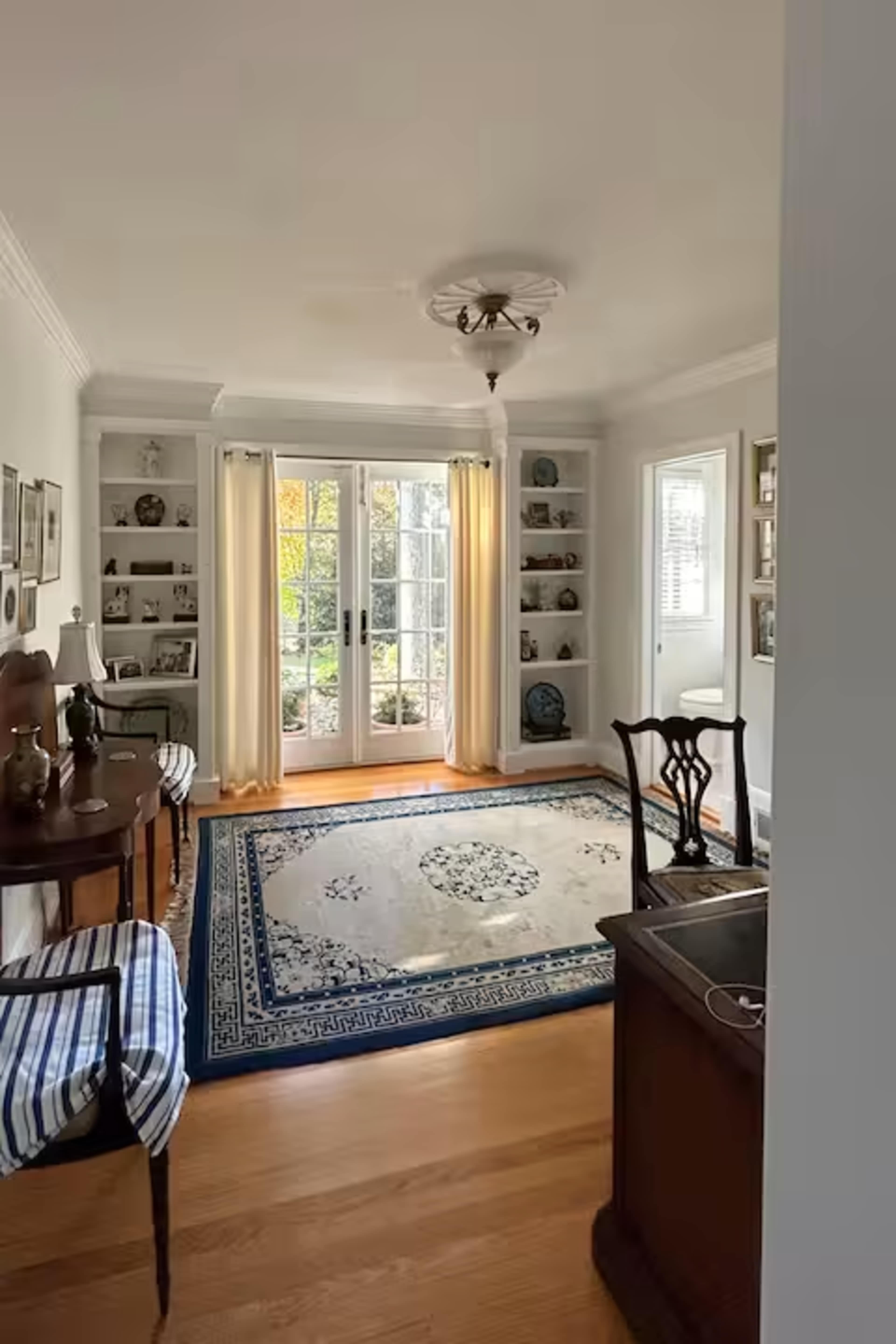 The image shows a well-lit living room featuring shelves with framed pictures, a decorative rug, and French doors leading to an outdoor area.