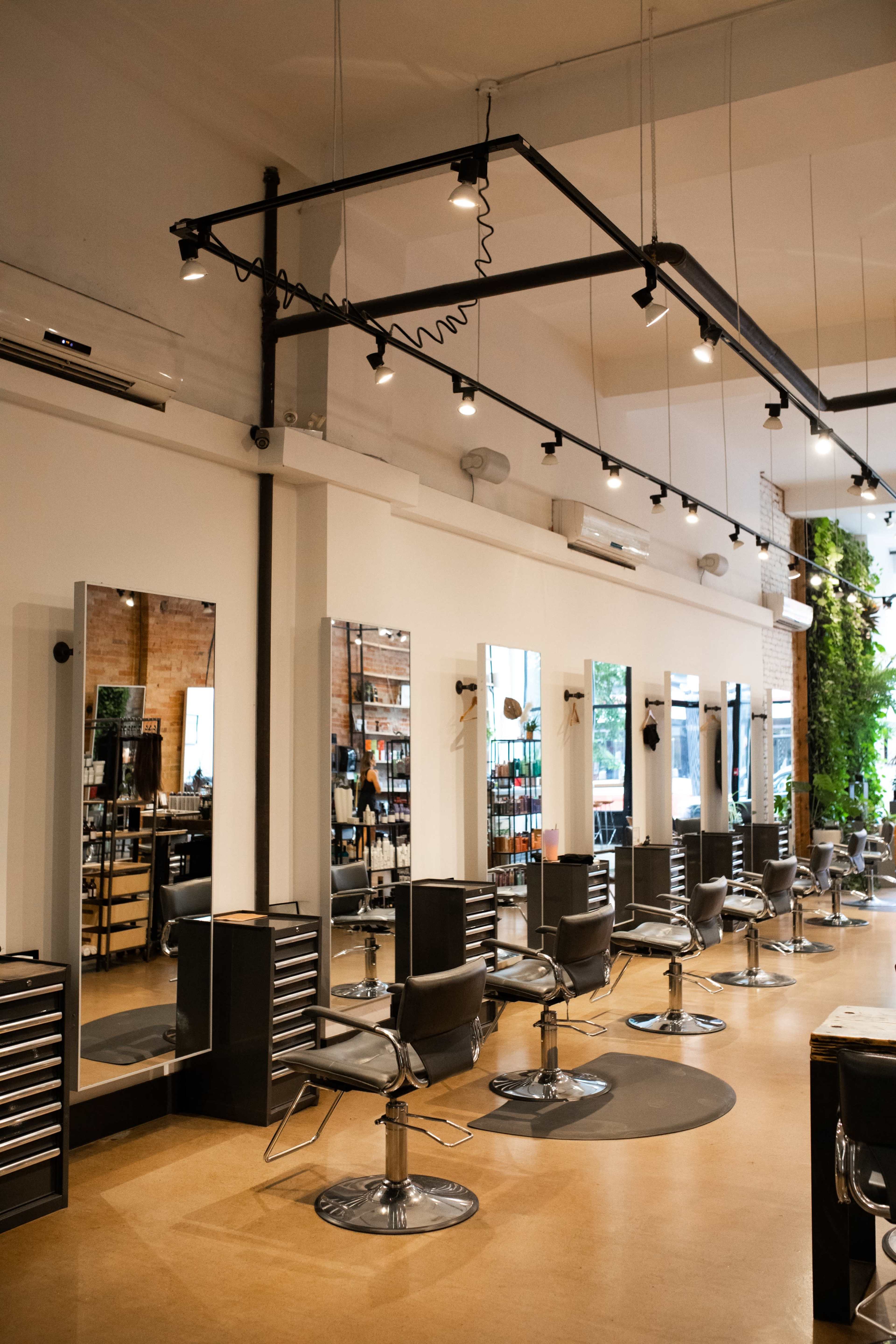 A modern hair salon featuring multiple styling stations with mirrors and adjustable salon chairs arranged in a spacious layout.