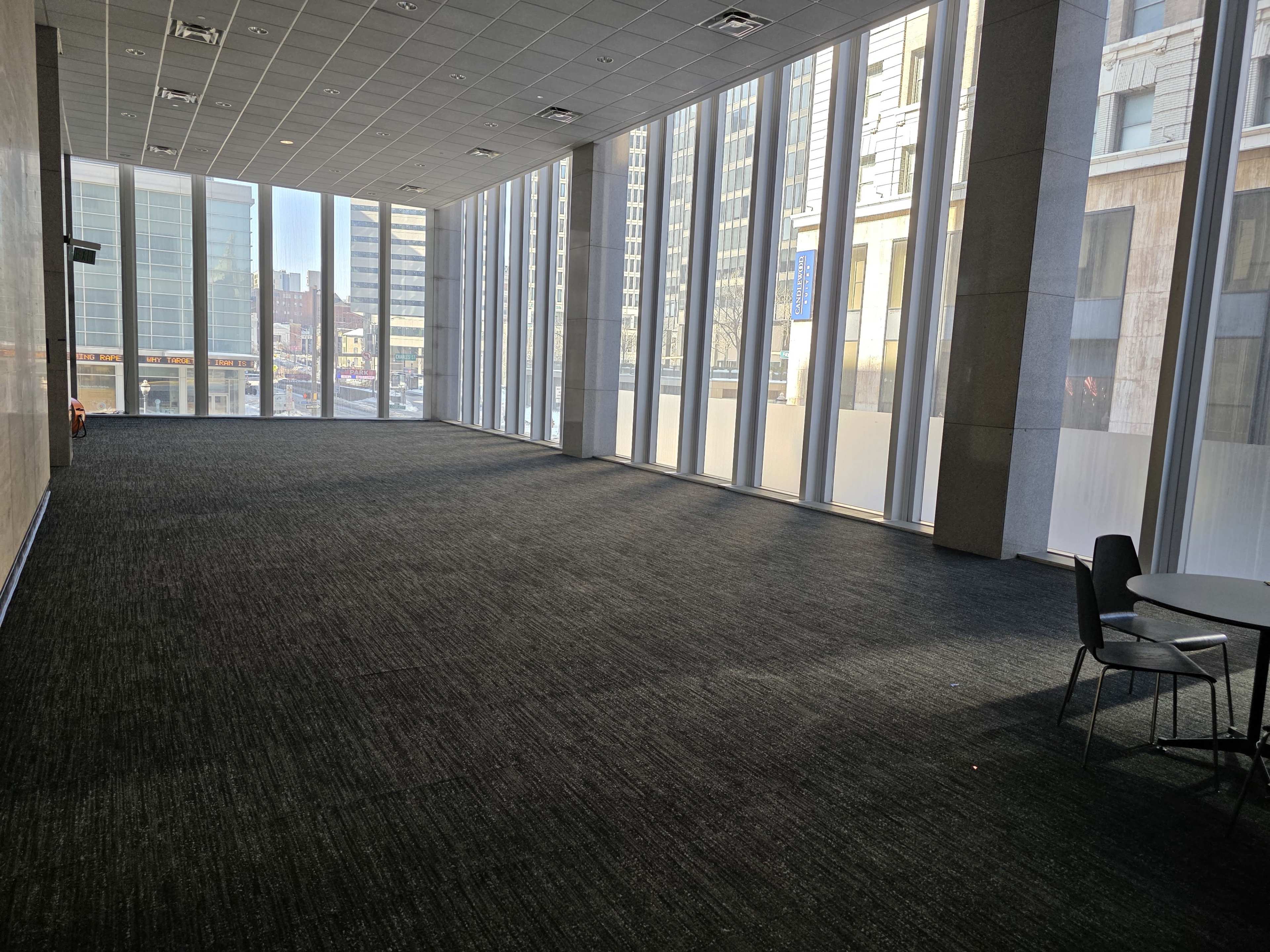 The image shows an empty room with large windows that allow natural light to fill the space, revealing a carpeted floor.