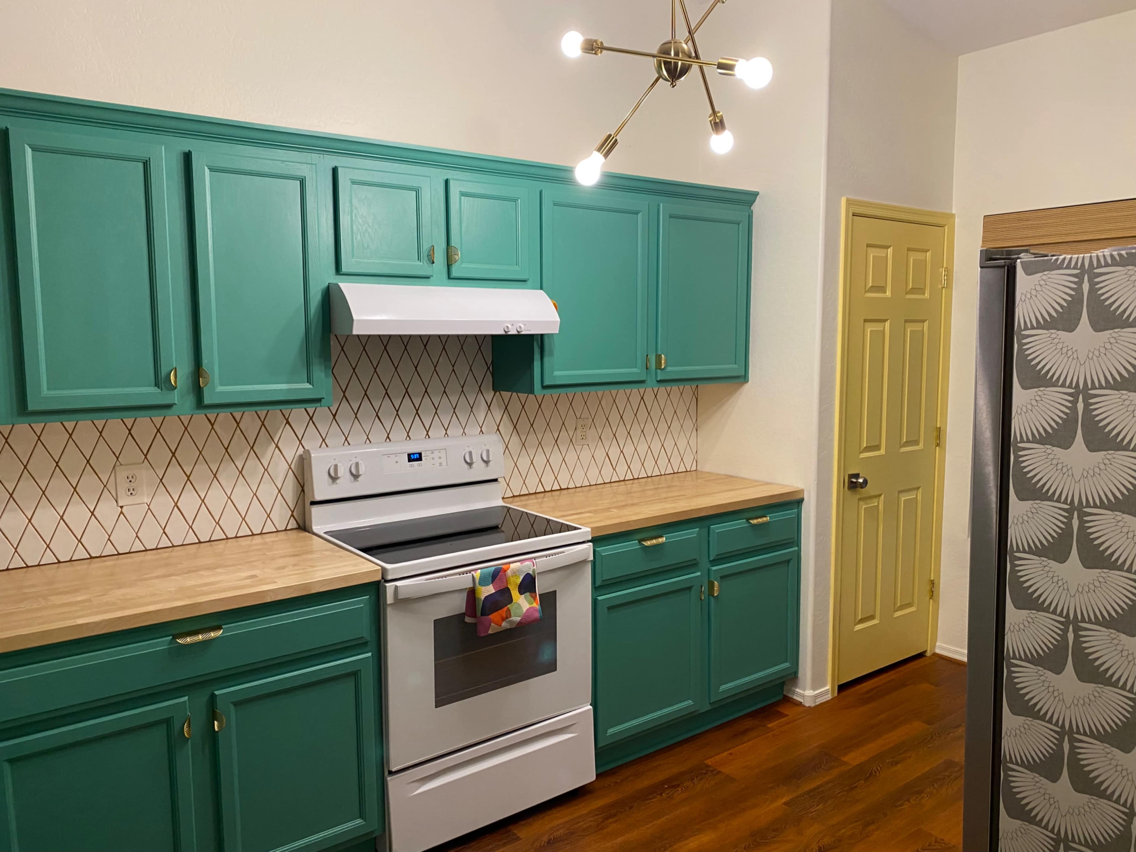A kitchen with teal cabinets, a white stove, a patterned backsplash, and wooden countertops.