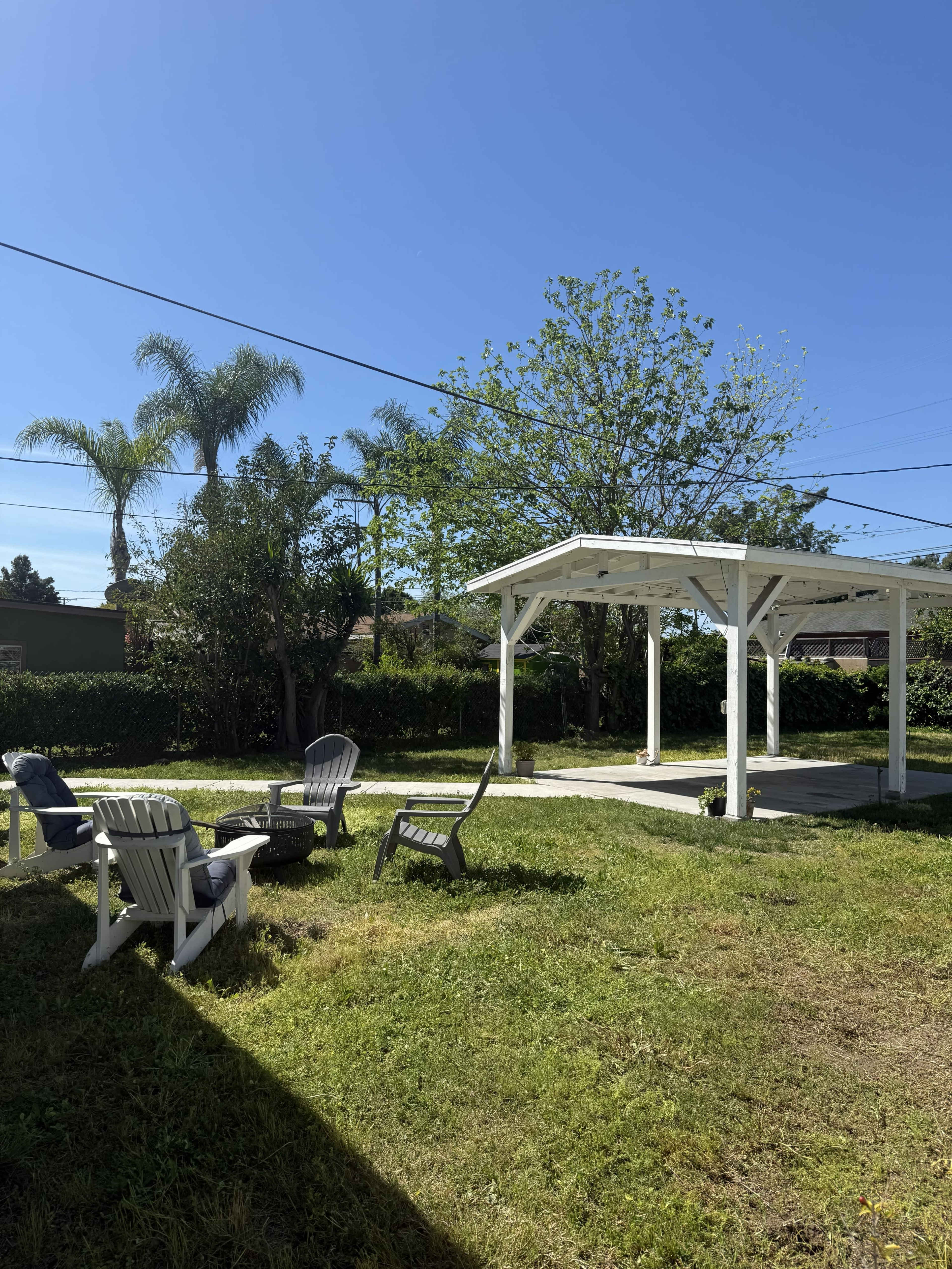 A spacious yard with several lounge chairs arranged around a covered patio under a clear blue sky.