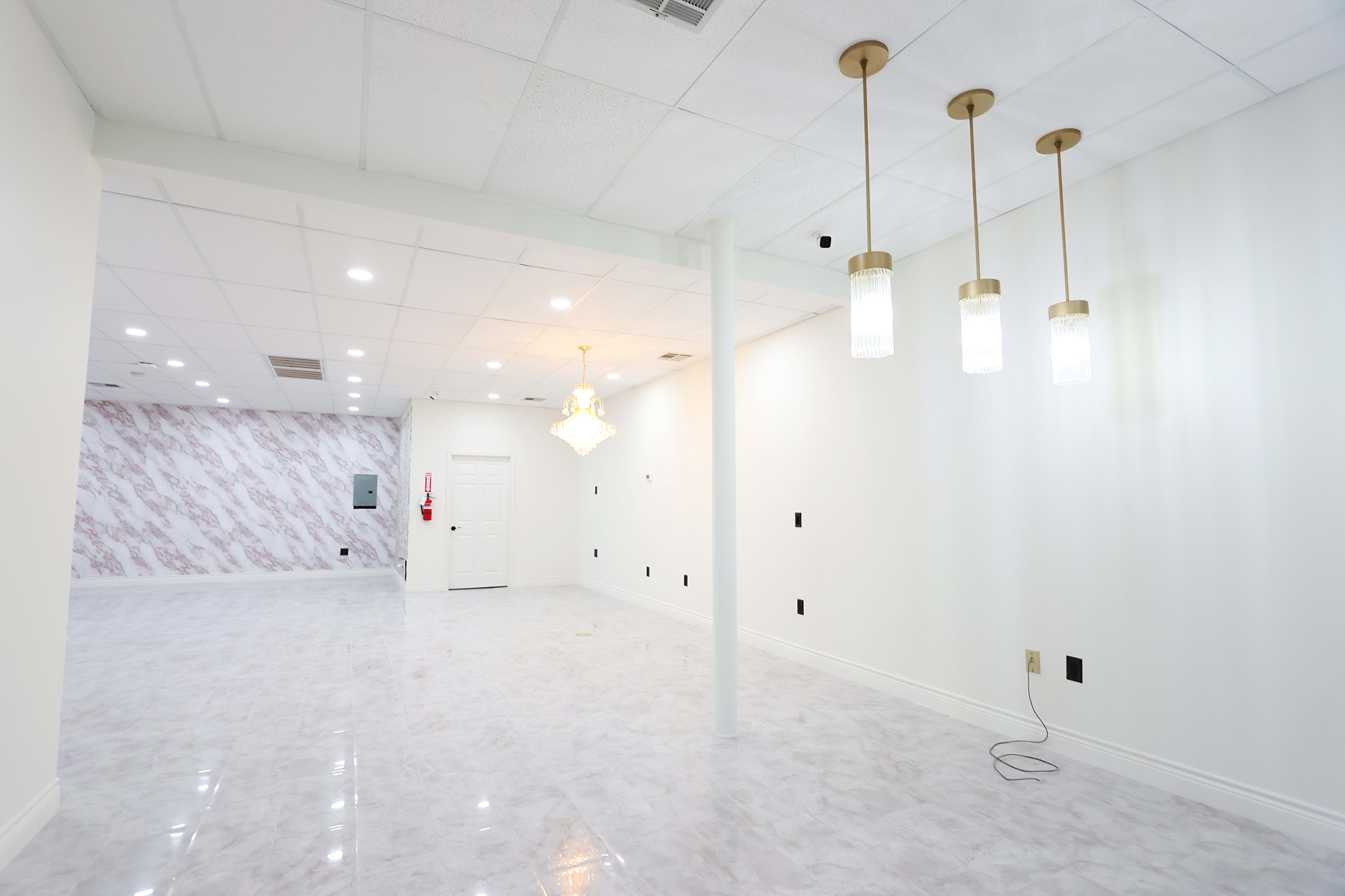 A spacious, well-lit interior of a room with white walls, a glossy floor, and modern light fixtures hanging from the ceiling.