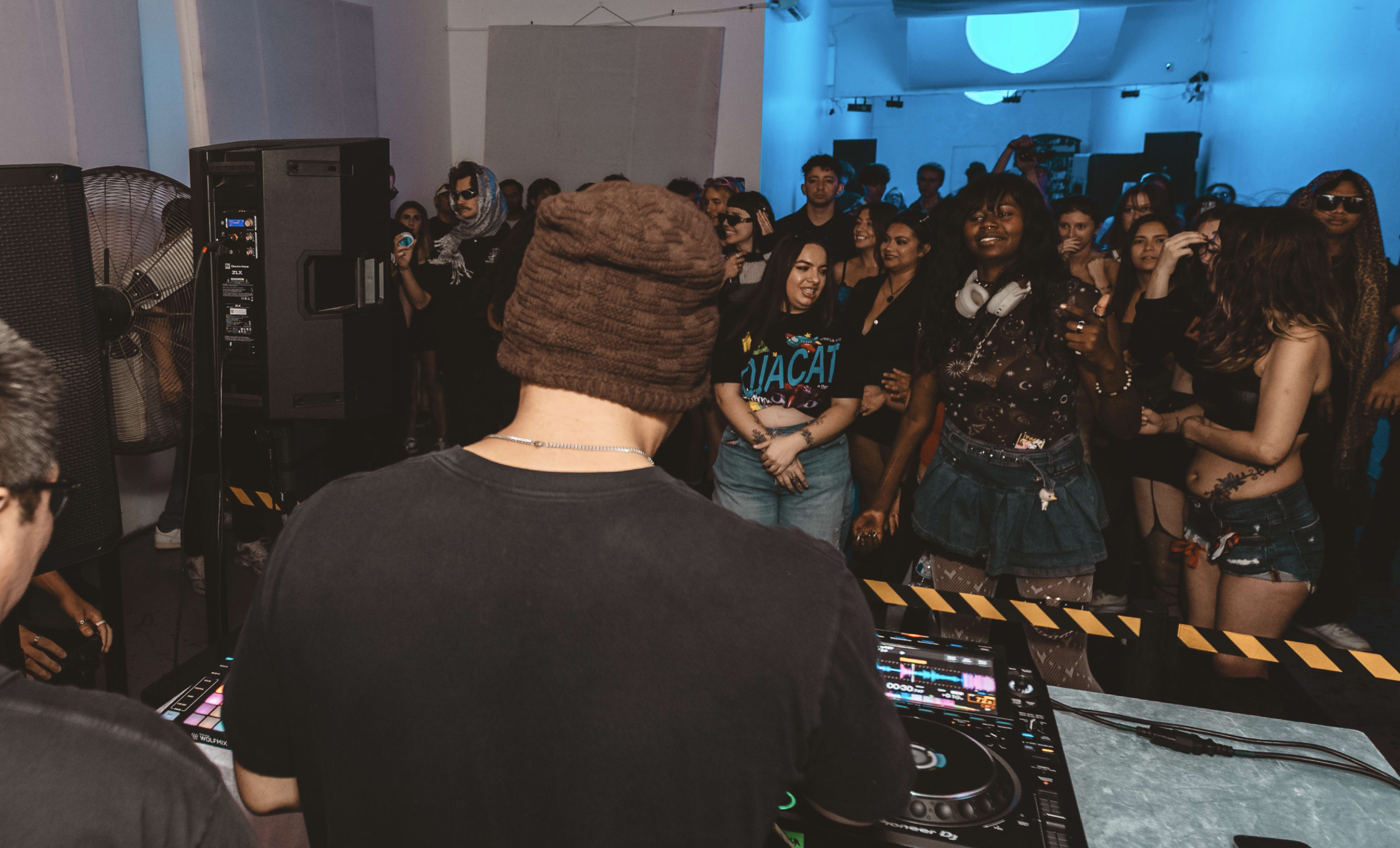 A DJ performs at a lively party while an engaged audience dances in front of him.